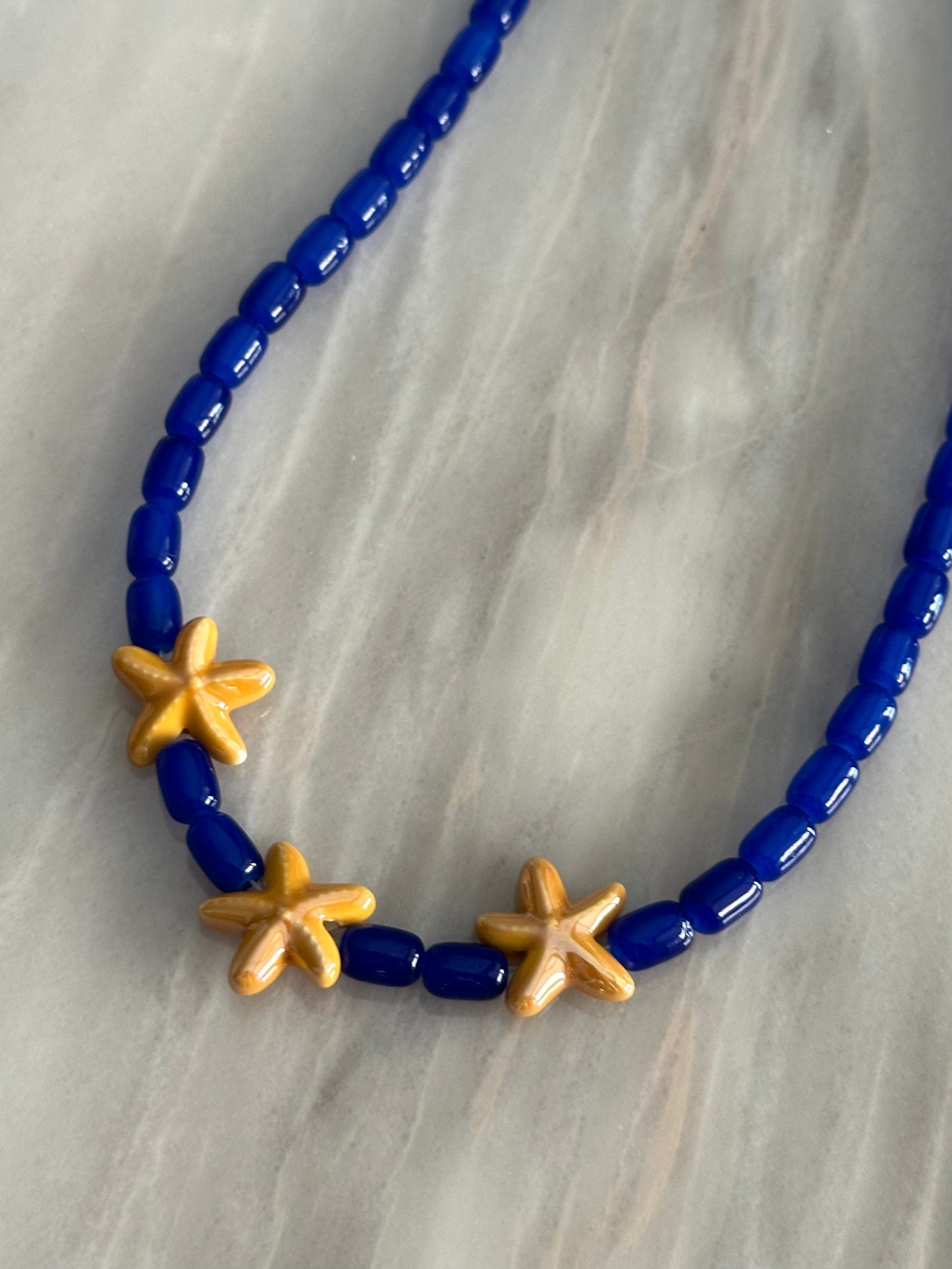 Collar hecho a mano con cuentas de cerámica en azul y tres estrellas de cerámica en amarillo en el centro. Con cierre ajustable en acero inoxidable