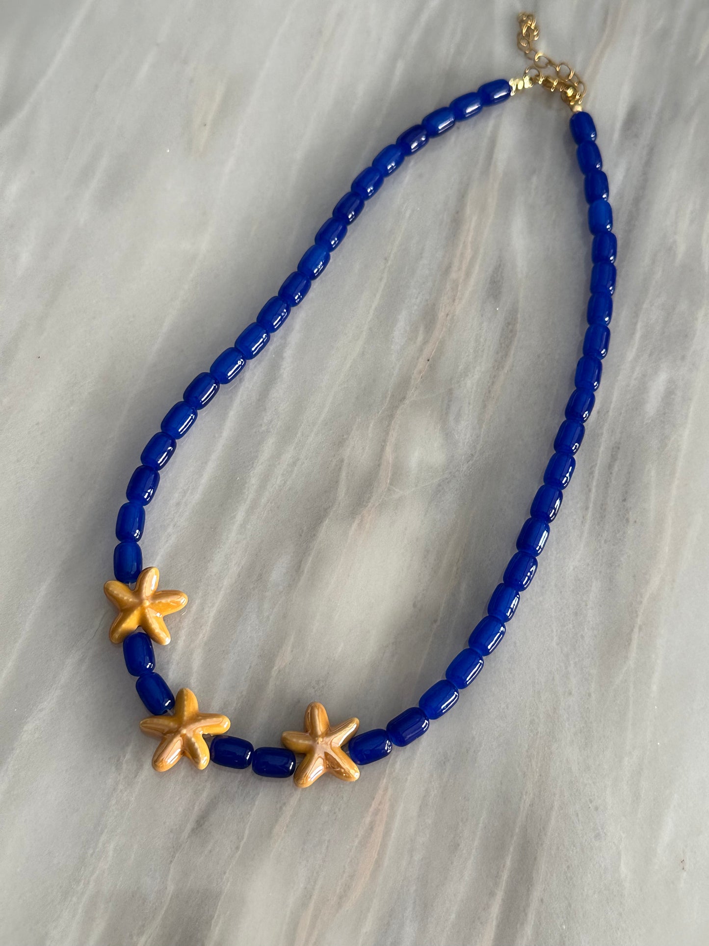 Collar hecho a mano con cuentas de cerámica en azul y tres estrellas de cerámica en amarillo en el centro. Con cierre ajustable en acero inoxidable