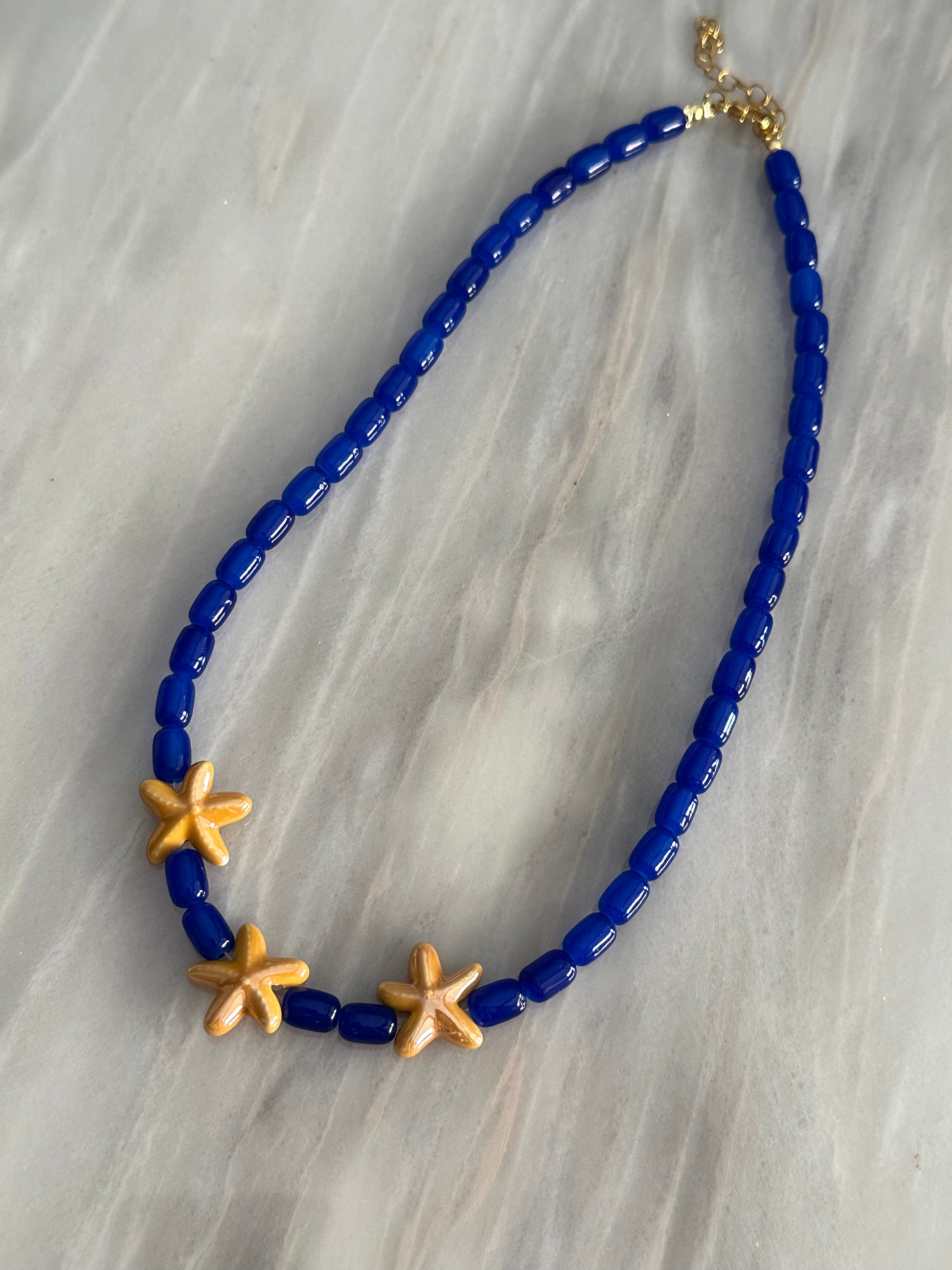 Collar hecho a mano con cuentas de cerámica en azul y tres estrellas de cerámica en amarillo en el centro. Con cierre ajustable en acero inoxidable