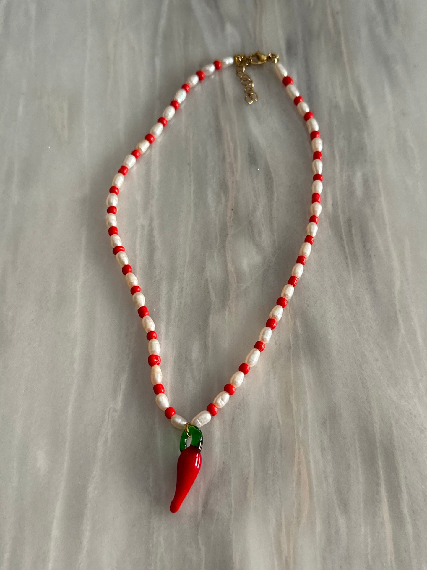 Collar hecho a mano con piedras de río y bolitas rojas, con un abalorio con forma de chili de cristal de murano en color rojo y verde