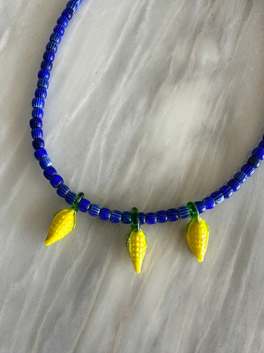 Collar hecho a mano con cuentas de cerámica azul y con tres abalorios con forma de mazorcas de maíz de cristal de murano en color amarillo. Cierre ajustable de acero inoxidable