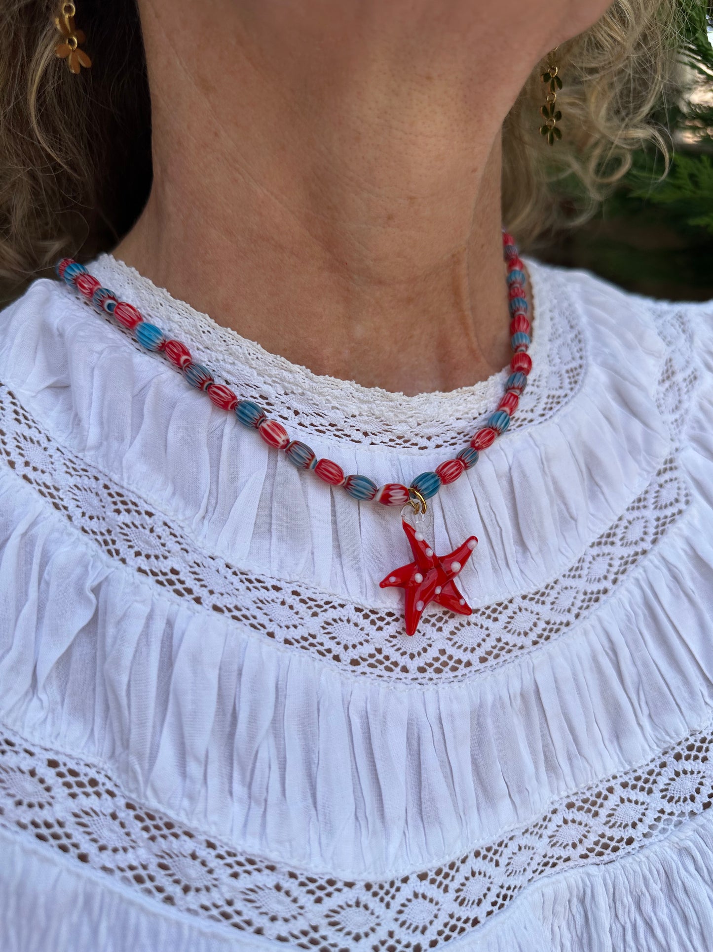 Collar hecho a mano con cuentas de cerámica azul y rojo con un abalorio con forma de estrella de mar de cristal de murano en color rojo. Cierre ajustable de acero inoxidable.
