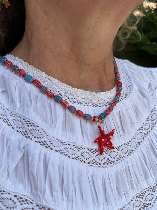 Collar hecho a mano con cuentas de cerámica azul y rojo con un abalorio con forma de estrella de mar de cristal de murano en color rojo. Cierre ajustable de acero inoxidable.