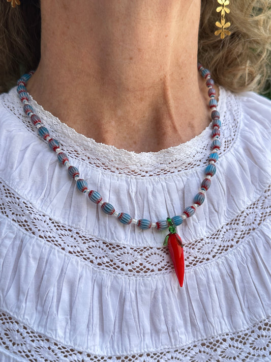 Collar hecho a mano con cuentas de cerámica azul y cuentas blancas con un abalorio con forma de chili de cristal de murano en color rojo y verde. Cierre ajustable de acero inoxidable.