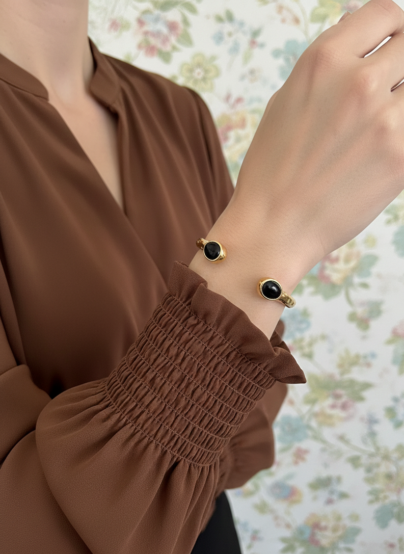 Brazalete de acero inoxidable con dos piedras negras, ajustable. En color dorado.