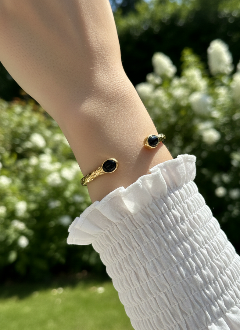 Brazalete de acero inoxidable con dos piedras negras, ajustable. En color dorado.