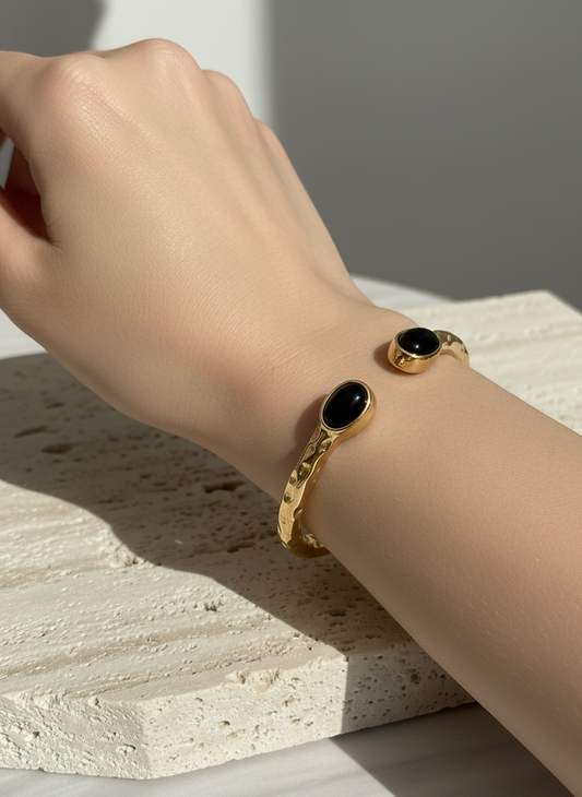 Brazalete de acero inoxidable con dos piedras negras, ajustable. En color dorado.