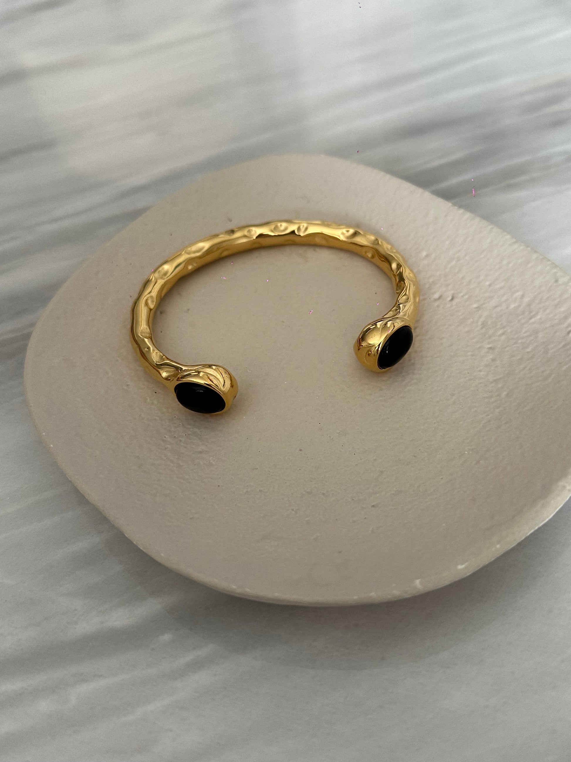 Brazalete de acero inoxidable con dos piedras negras, ajustable. En color dorado.