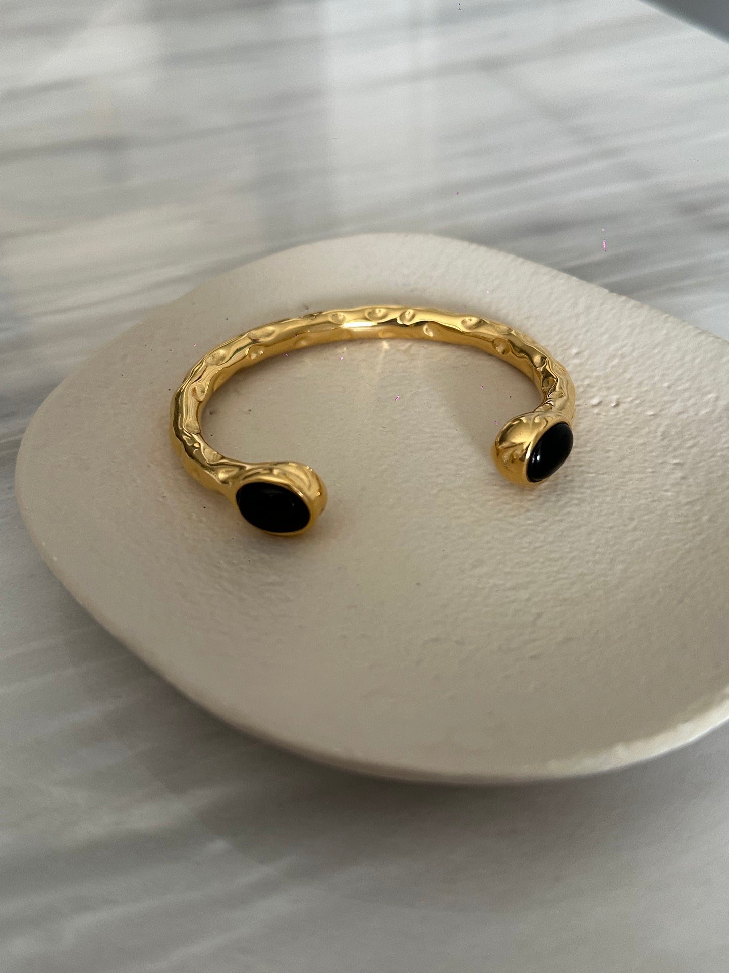 Brazalete de acero inoxidable con dos piedras negras, ajustable. En color dorado.