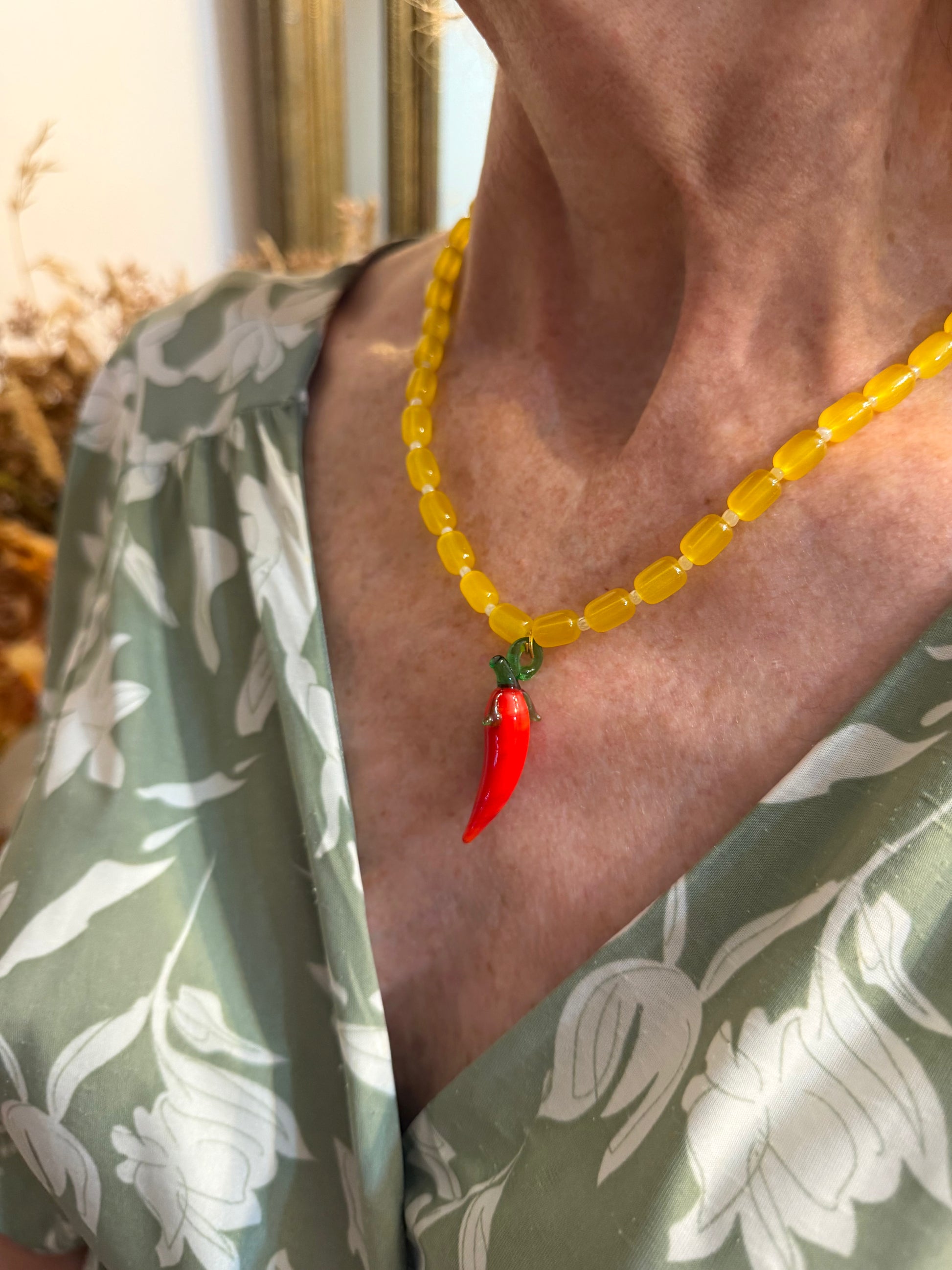 Collar hecho a mano con cuentas de cerámica amarilla y bolitas blancas, con un abalorio con forma de chili de cristal de murano en color rojo y verde. Cierre ajustable