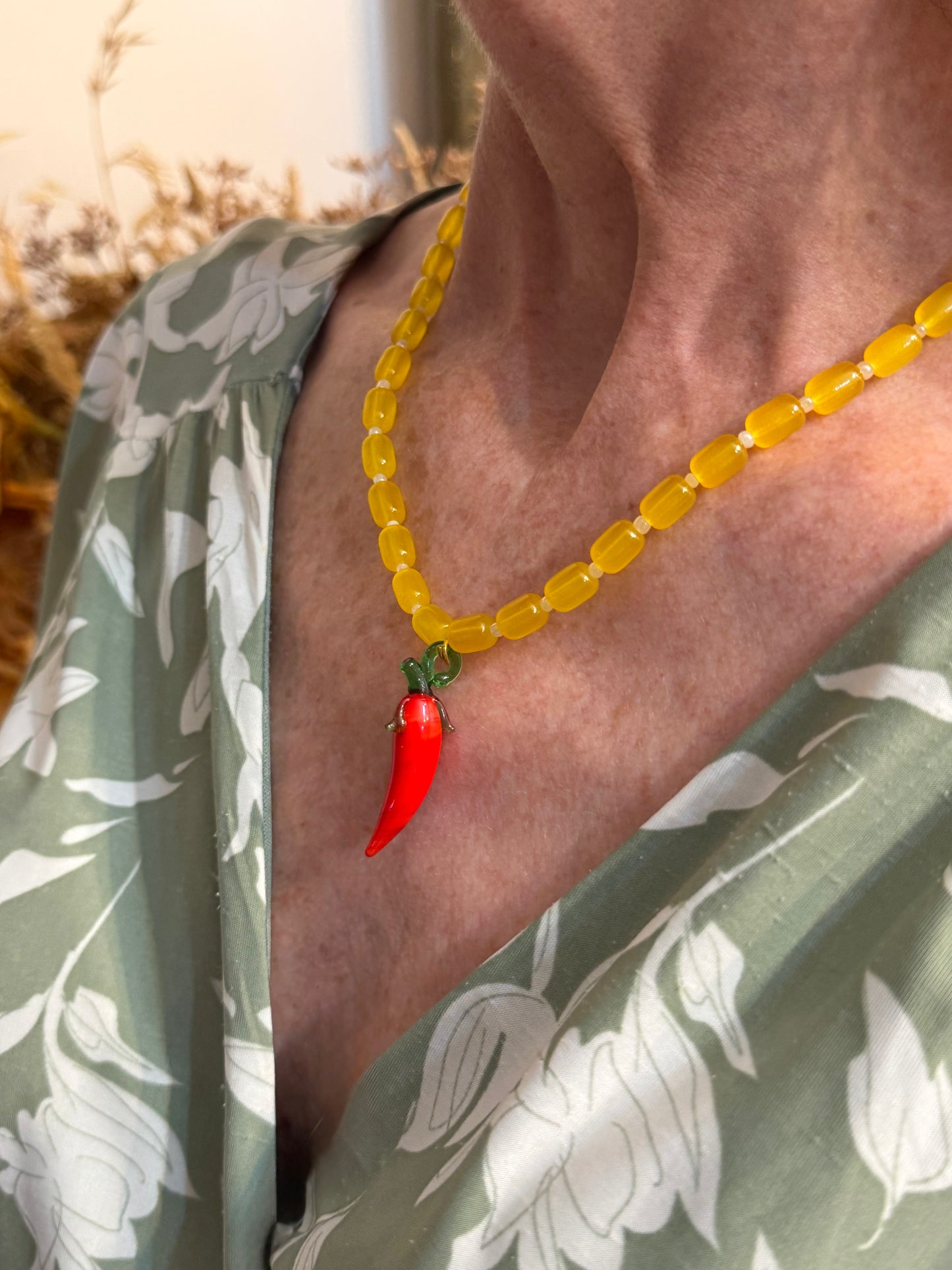 Collar hecho a mano con cuentas de cerámica amarilla y bolitas blancas, con un abalorio con forma de chili de cristal de murano en color rojo y verde. Cierre ajustable