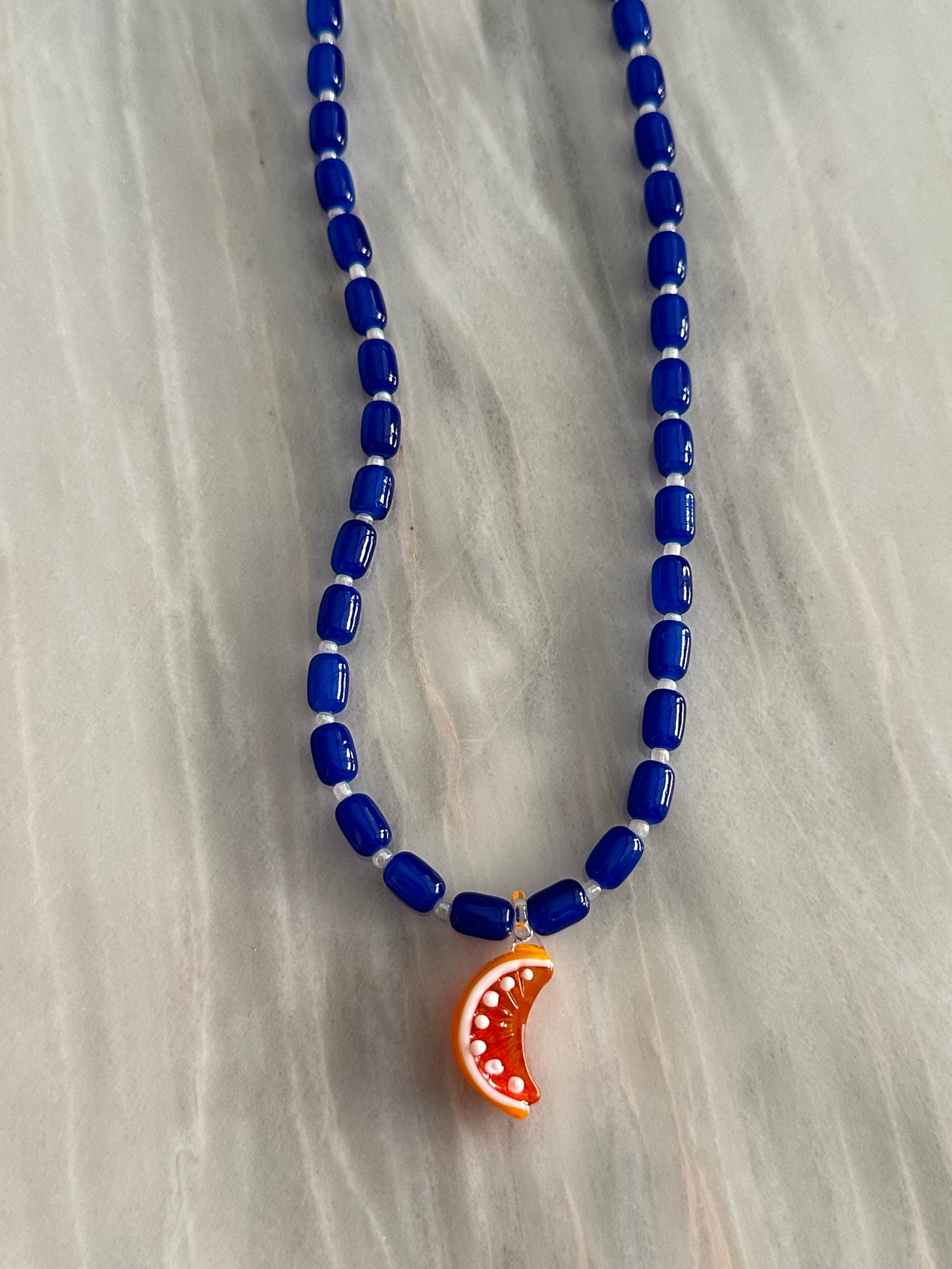 Collar hecho a mano con bolas de cerámica en azul oscuro y con un abalorio de cristal de murano con forma de gajo de naranja. Con cierre ajustable de acero inoxidable