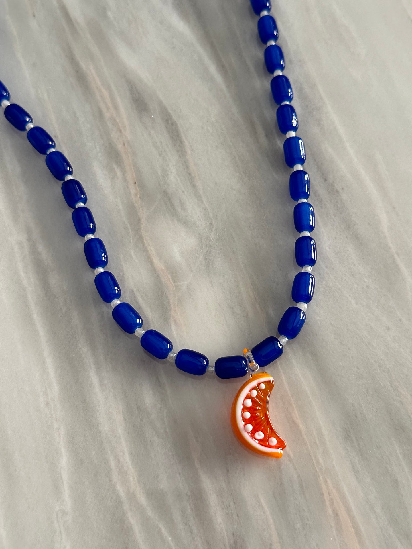 Collar hecho a mano con bolas de cerámica en azul oscuro y con un abalorio de cristal de murano con forma de gajo de naranja. Con cierre ajustable de acero inoxidable