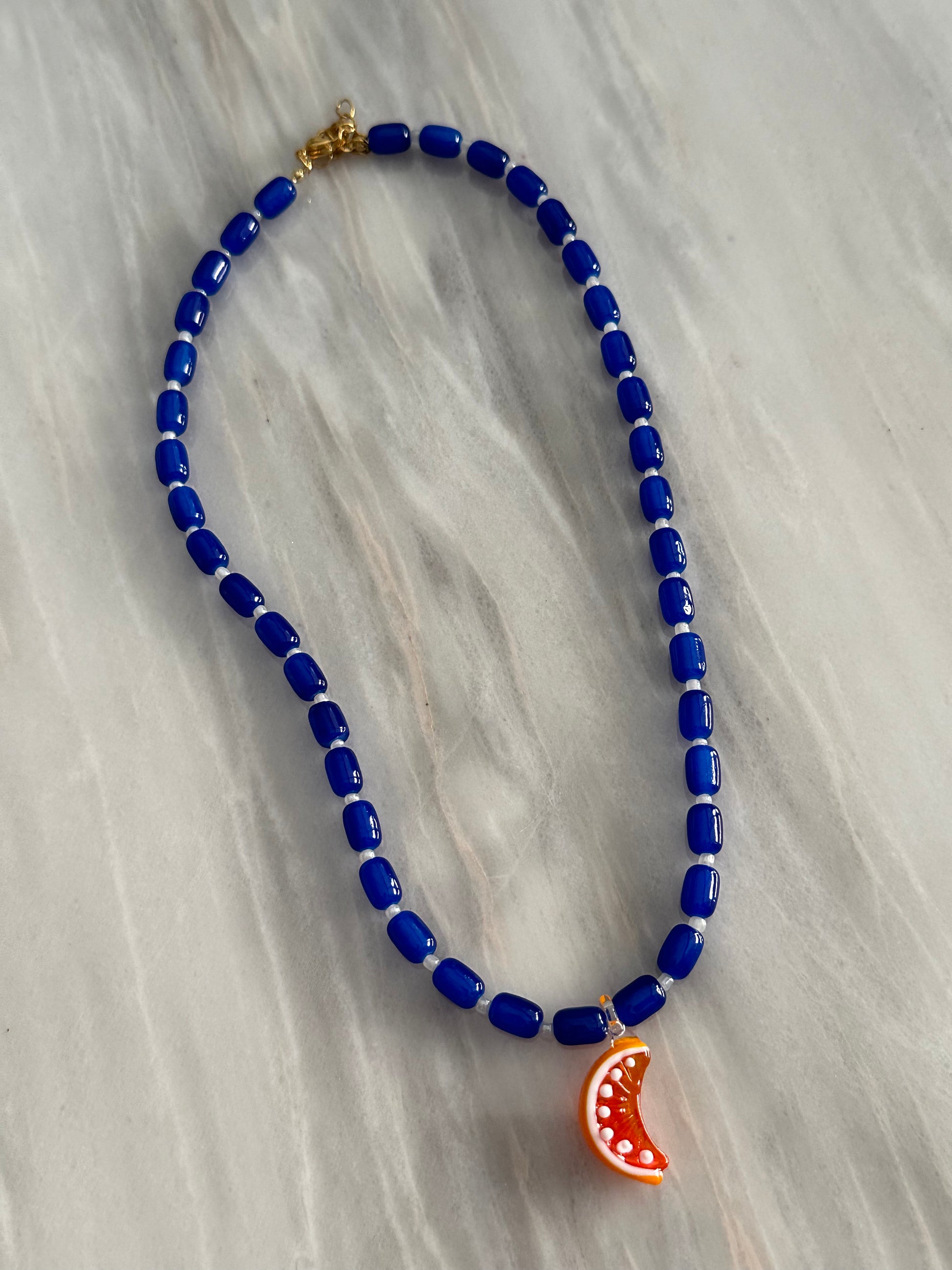 Collar hecho a mano con bolas de cerámica en azul oscuro y con un abalorio de cristal de murano con forma de gajo de naranja. Con cierre ajustable de acero inoxidable