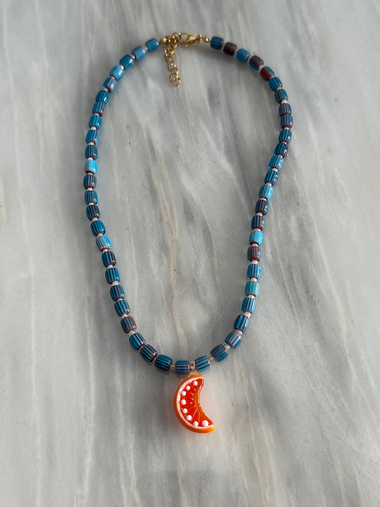 Collar hecho a mano con bolas de cerámica, boitas blancas y con un abalorio de cristal de murano con forma de gajo de naranja. Con cierre ajustable de acero inoxidable