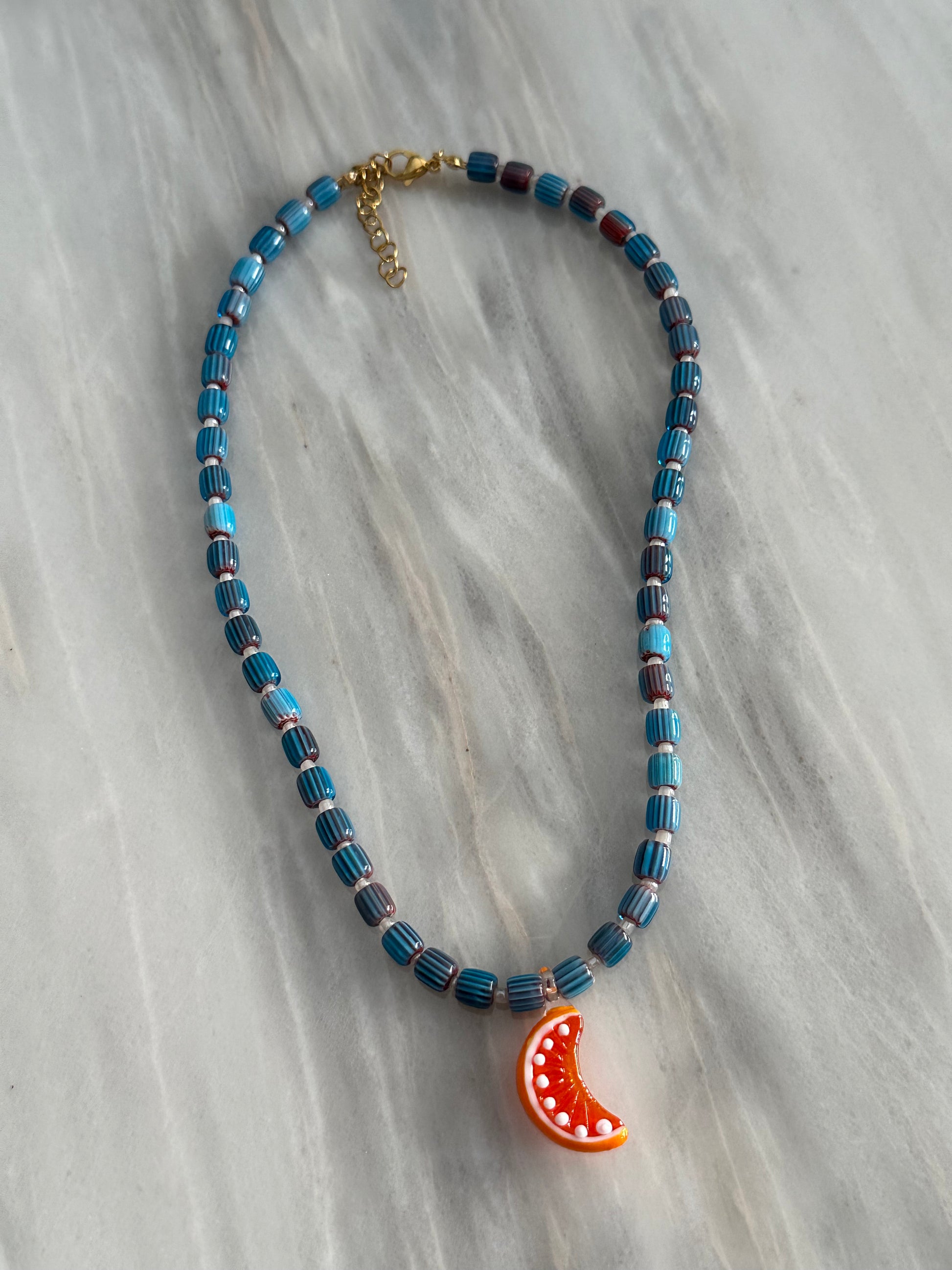 Collar hecho a mano con bolas de cerámica, boitas blancas y con un abalorio de cristal de murano con forma de gajo de naranja. Con cierre ajustable de acero inoxidable