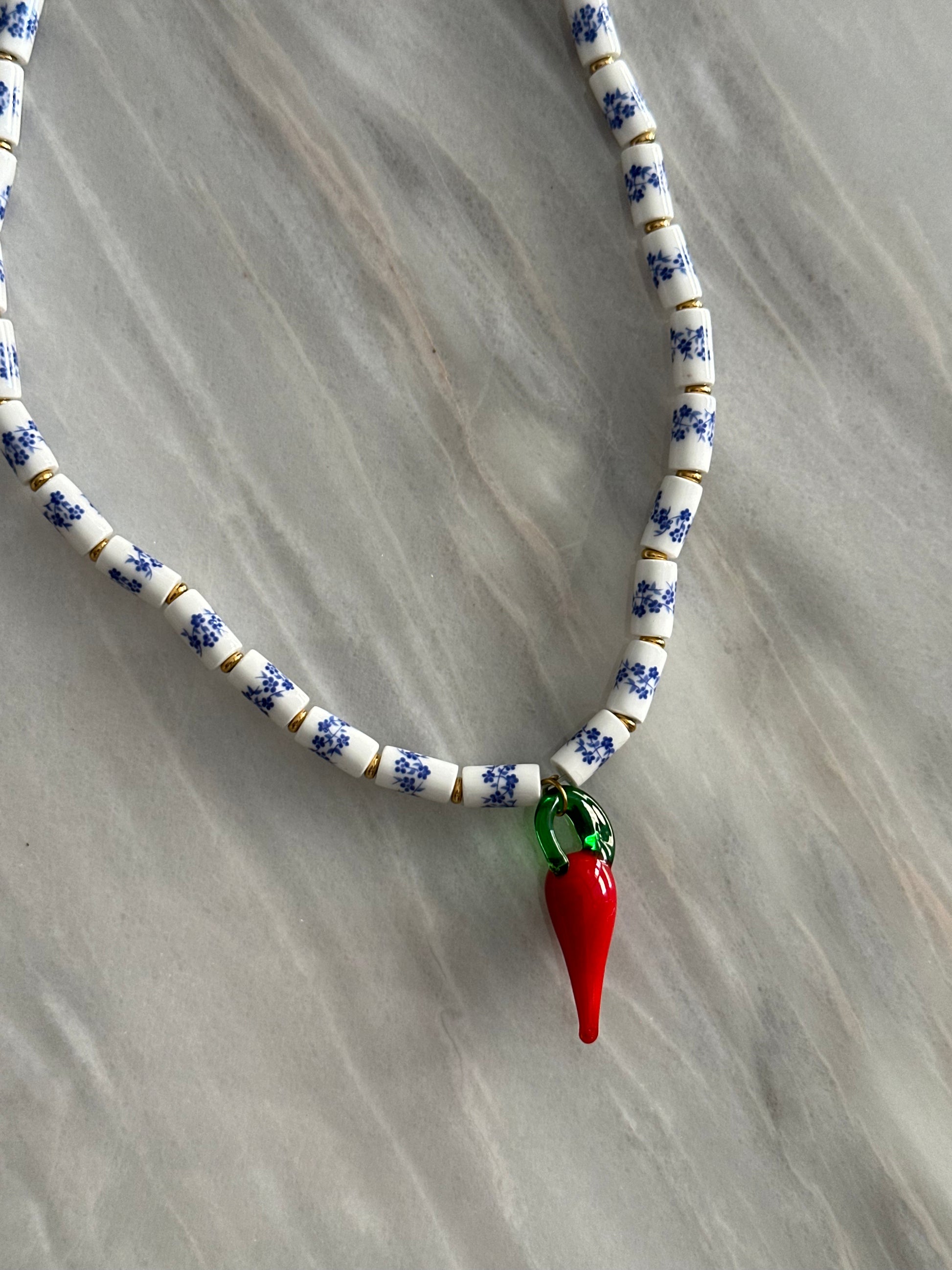 Collar hecho a mano con cuentas de porcelana con flores azules, con un abalorio con forma de chili de cristal de murano en rojo y verde