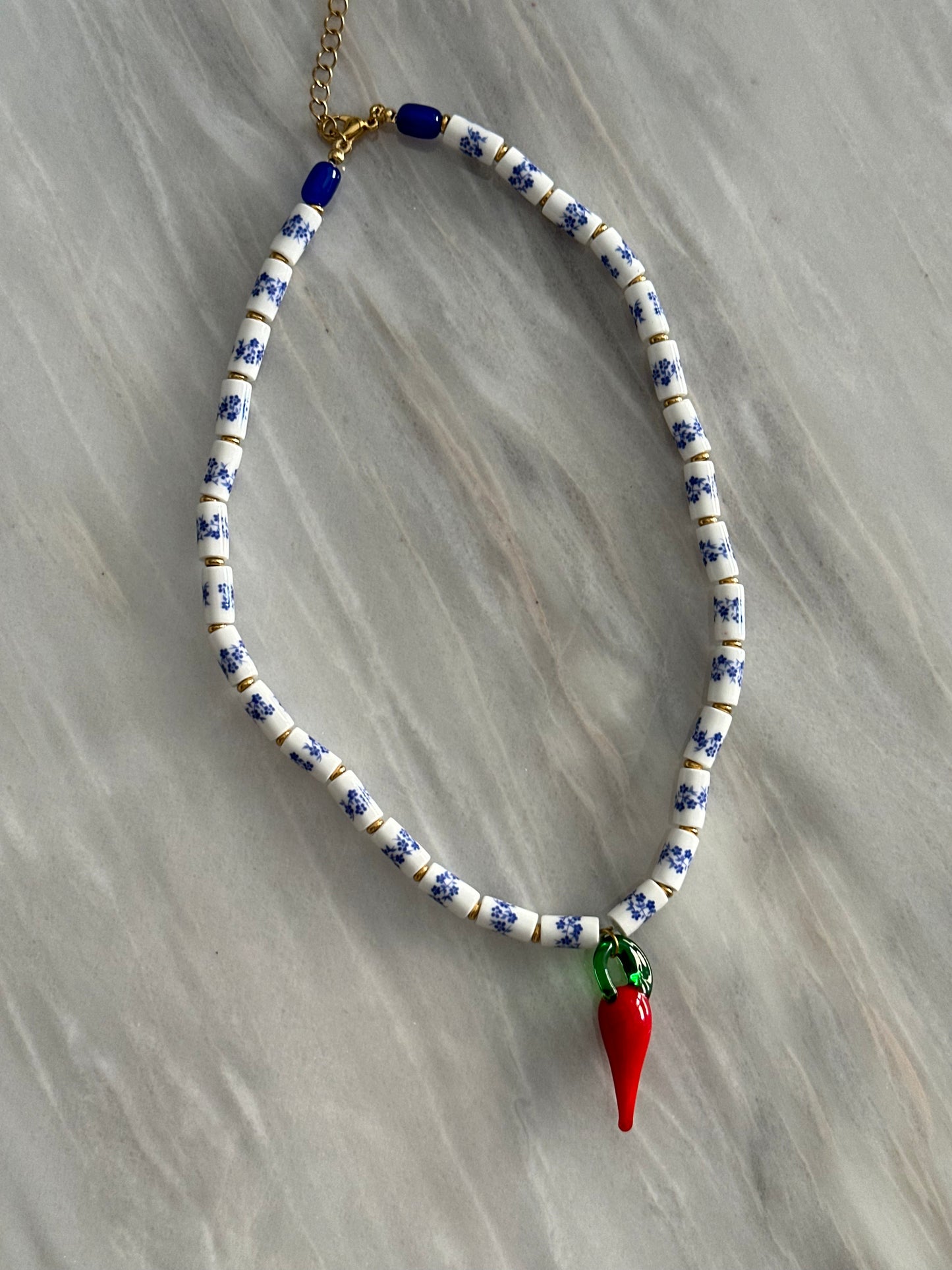 Collar hecho a mano con cuentas de porcelana con flores azules, con un abalorio con forma de chili de cristal de murano en rojo y verde