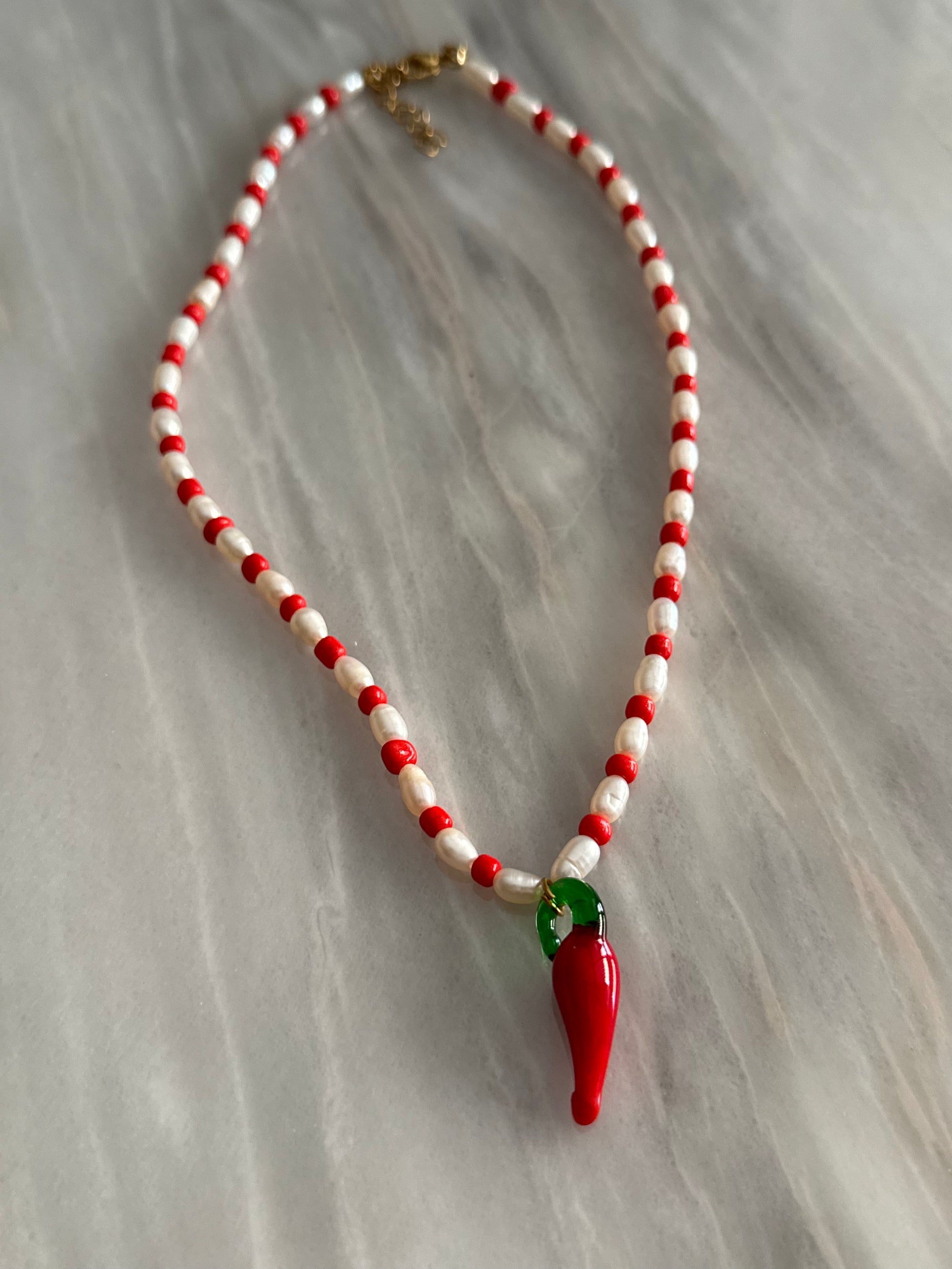 Collar hecho a mano con piedras de río y bolitas rojas, con un abalorio con forma de chili de cristal de murano en color rojo y verde