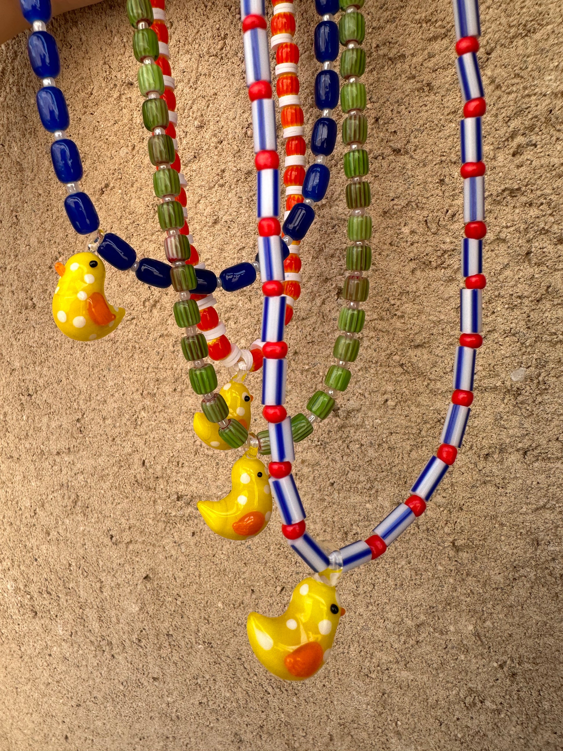 Collar hecho a mano con cerámica verde, cuentas blancas y con un abalorio de cristal de murano con forma de pollito en color amarillo. Con cierre ajustable de acero inoxidable