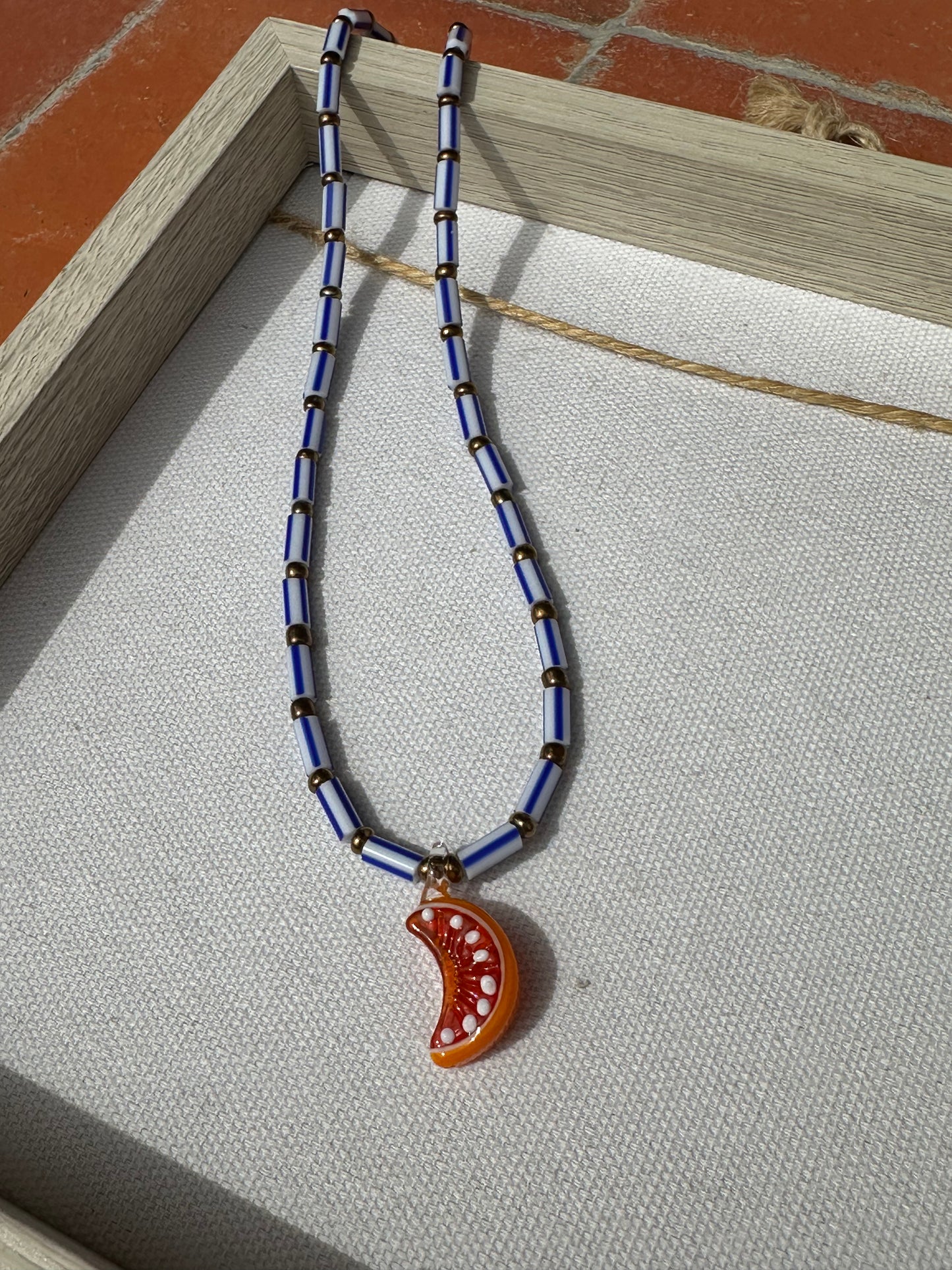 Collar hecho a mano con cuentas rayadas en azul, bolitas doradas y con un abalorio de cristal de murano con forma de gajo de naranja. Con cierre ajustable de acero inoxidable