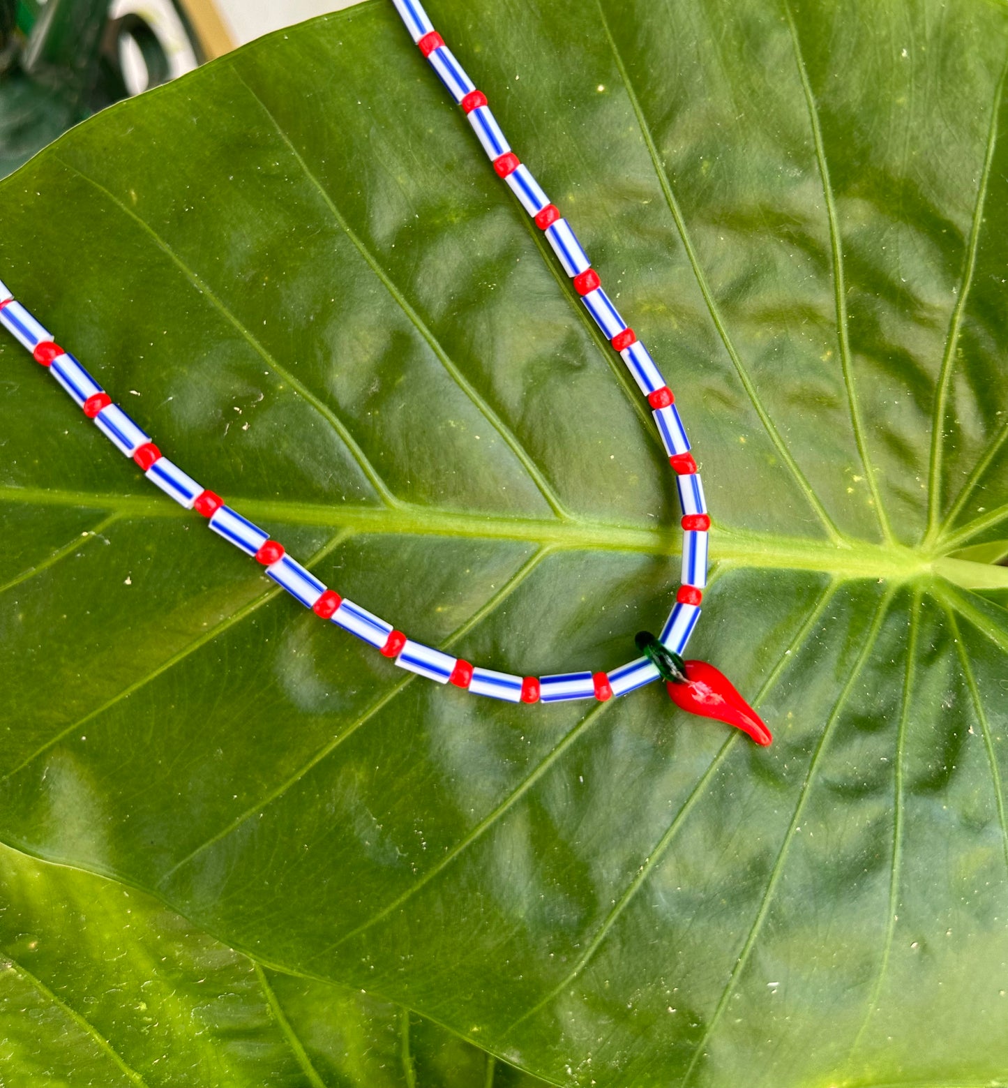 Collar hecho a mano con cuentas rayadas en azul, bolitas rojas y con un abalorio de cristal de murano con forma de chili. Con cierre ajustable de acero inoxidable