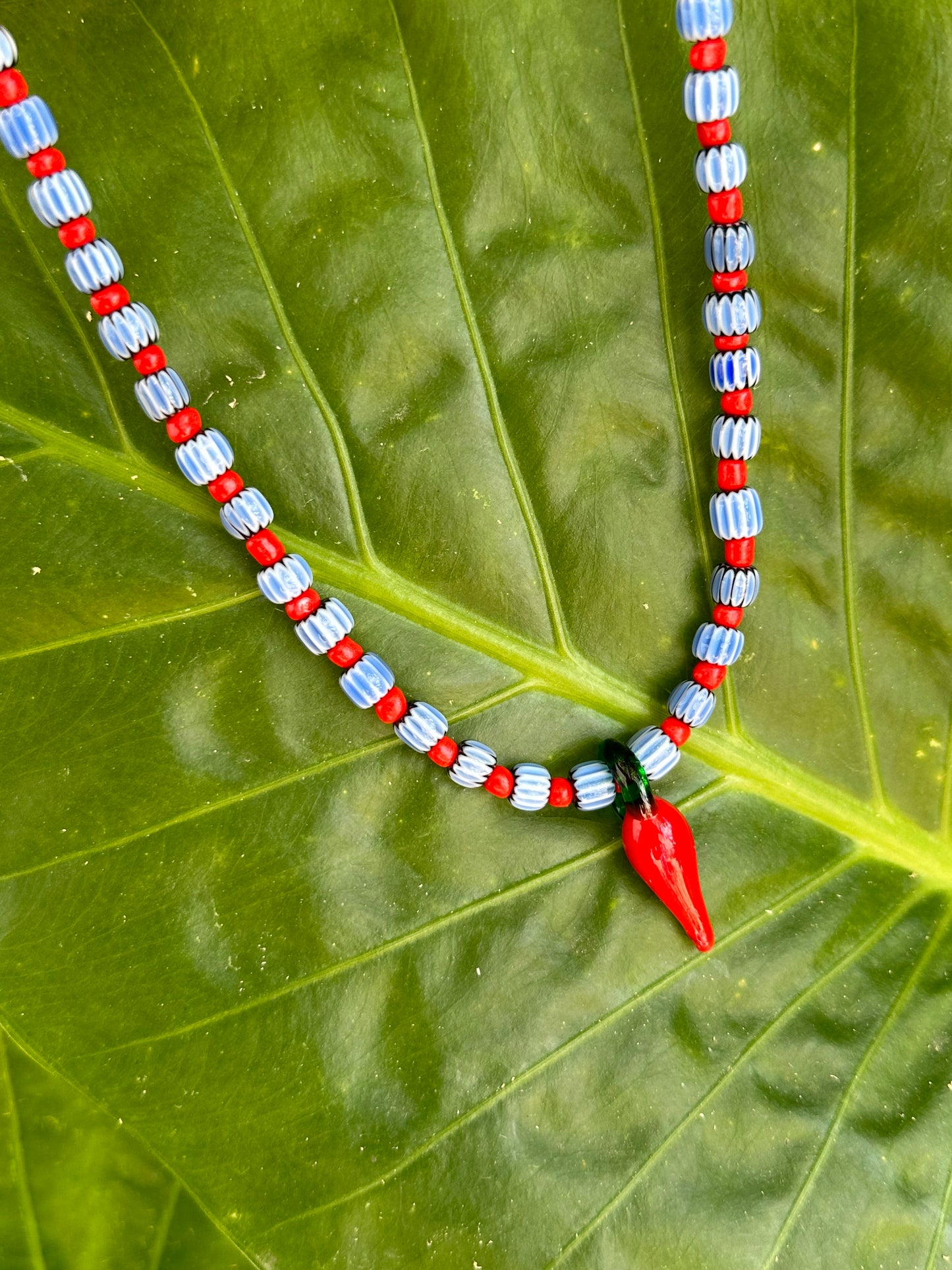 Collar hecho a mano con cuentas de cerámica azul y bolitas rojas, con un abalorio con forma de chili de cristal de murano en color rojo y verde. Cierre ajustable