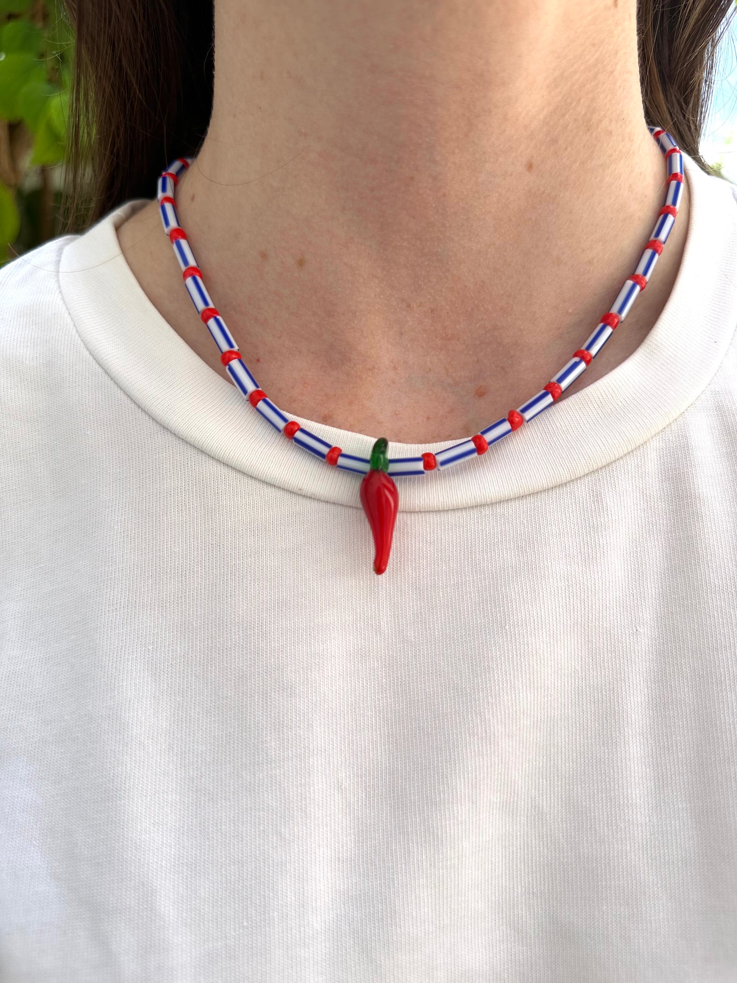 Collar hecho a mano con cuentas rayadas en azul, bolitas rojas y con un abalorio de cristal de murano con forma de chili. Con cierre ajustable de acero inoxidable