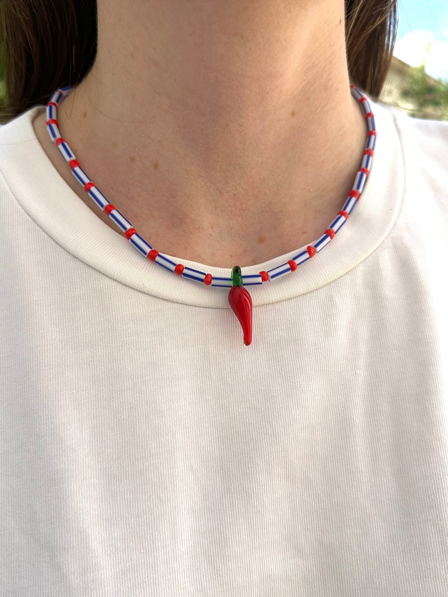 Collar hecho a mano con cuentas rayadas en azul, bolitas rojas y con un abalorio de cristal de murano con forma de chili. Con cierre ajustable de acero inoxidable