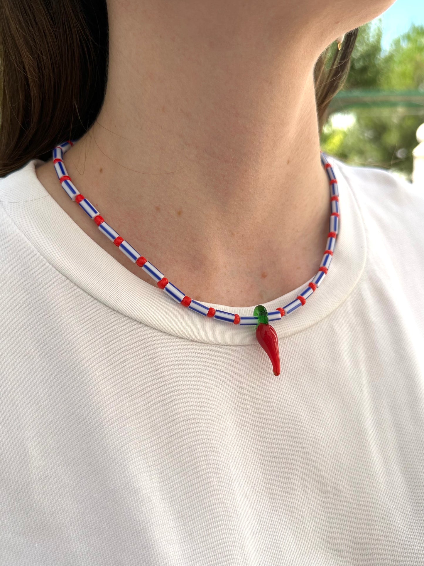 Collar hecho a mano con cuentas rayadas en azul, bolitas rojas y con un abalorio de cristal de murano con forma de chili. Con cierre ajustable de acero inoxidable