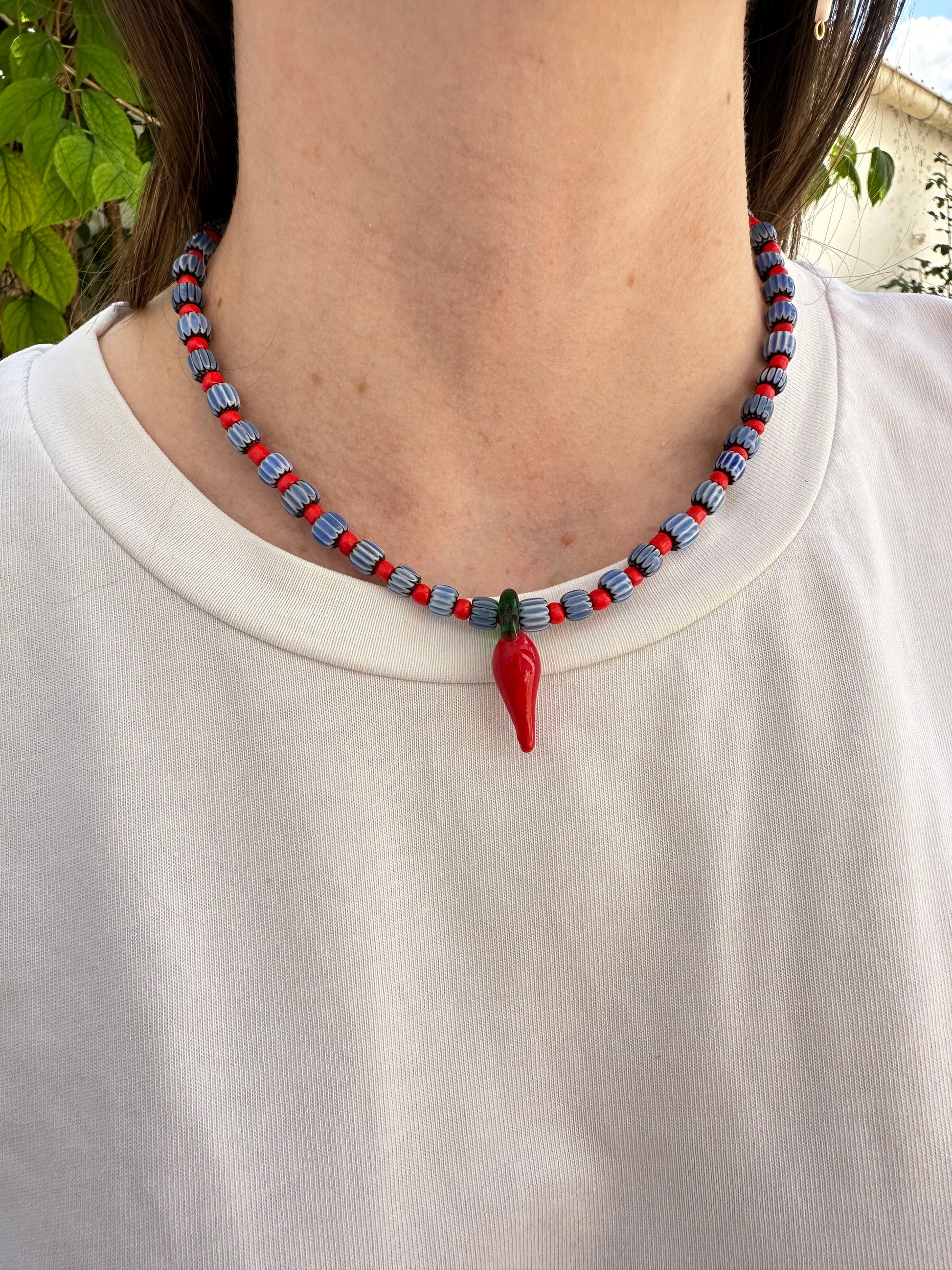 Collar hecho a mano con cuentas de cerámica azul y bolitas rojas, con un abalorio con forma de chili de cristal de murano en color rojo y verde. Cierre ajustable