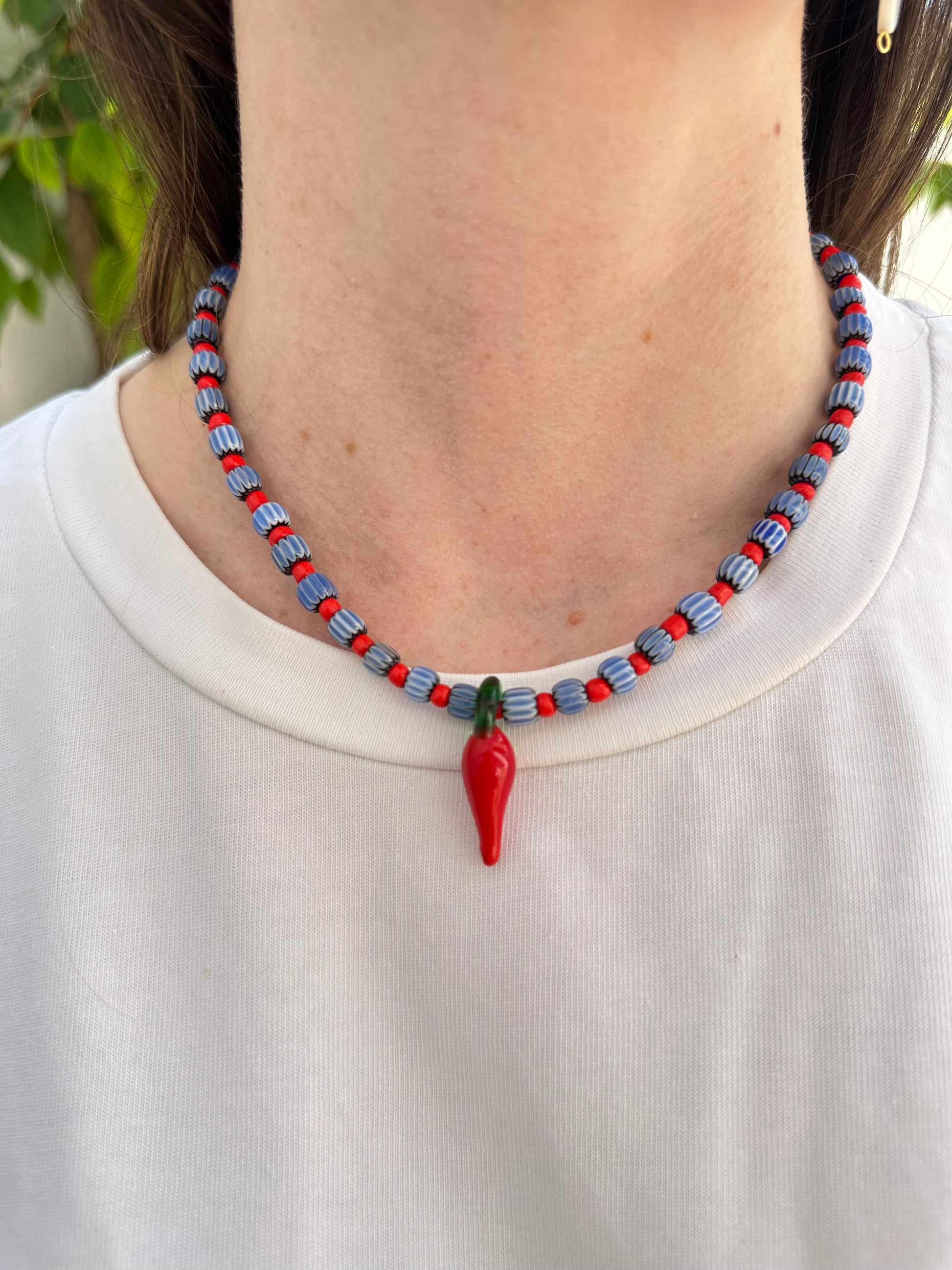 Collar hecho a mano con cuentas de cerámica azul y bolitas rojas, con un abalorio con forma de chili de cristal de murano en color rojo y verde. Cierre ajustable