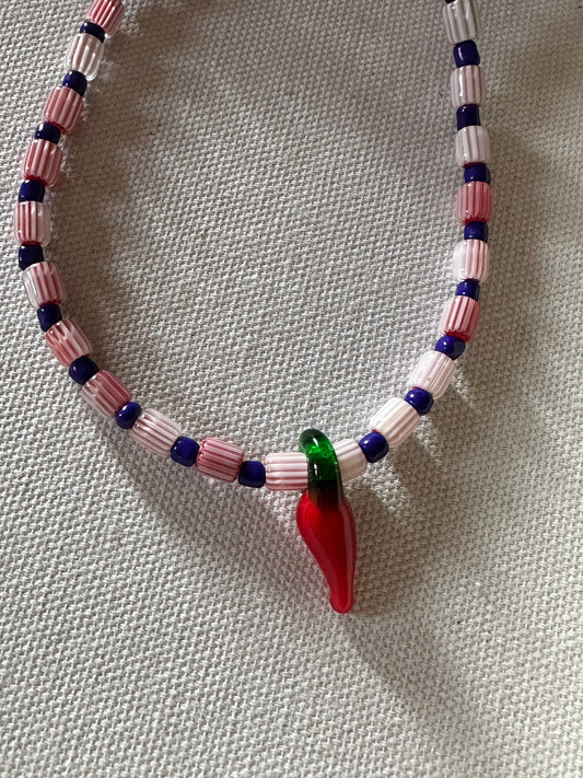 Collar hecho a mano con cuentas de cerámica blancas y cuentas azules, con un abalorio con forma de chili de cristal de murano en color rojo y verde. Cierre ajustable