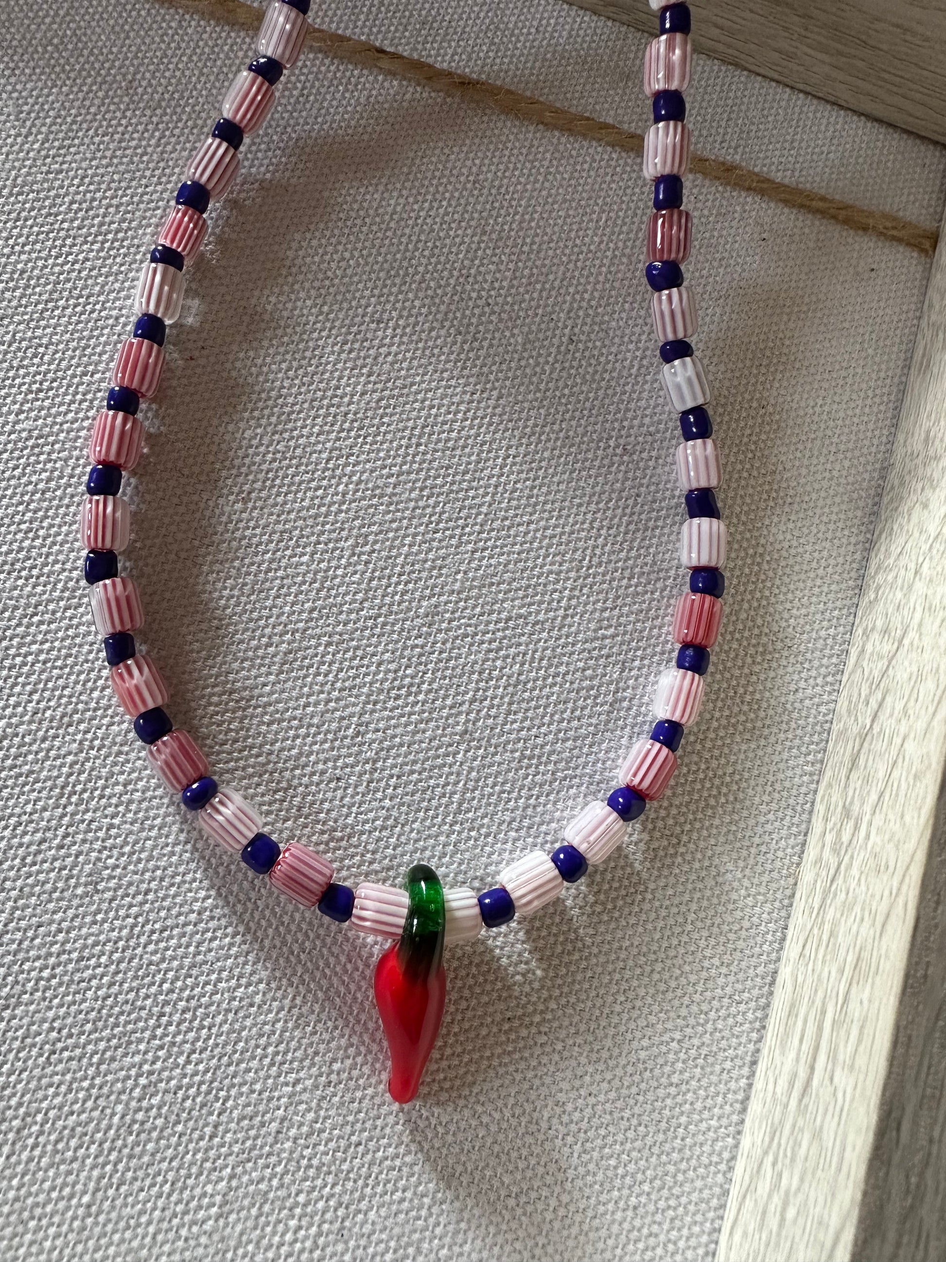 Collar hecho a mano con cuentas de cerámica blancas y cuentas azules, con un abalorio con forma de chili de cristal de murano en color rojo y verde. Cierre ajustable