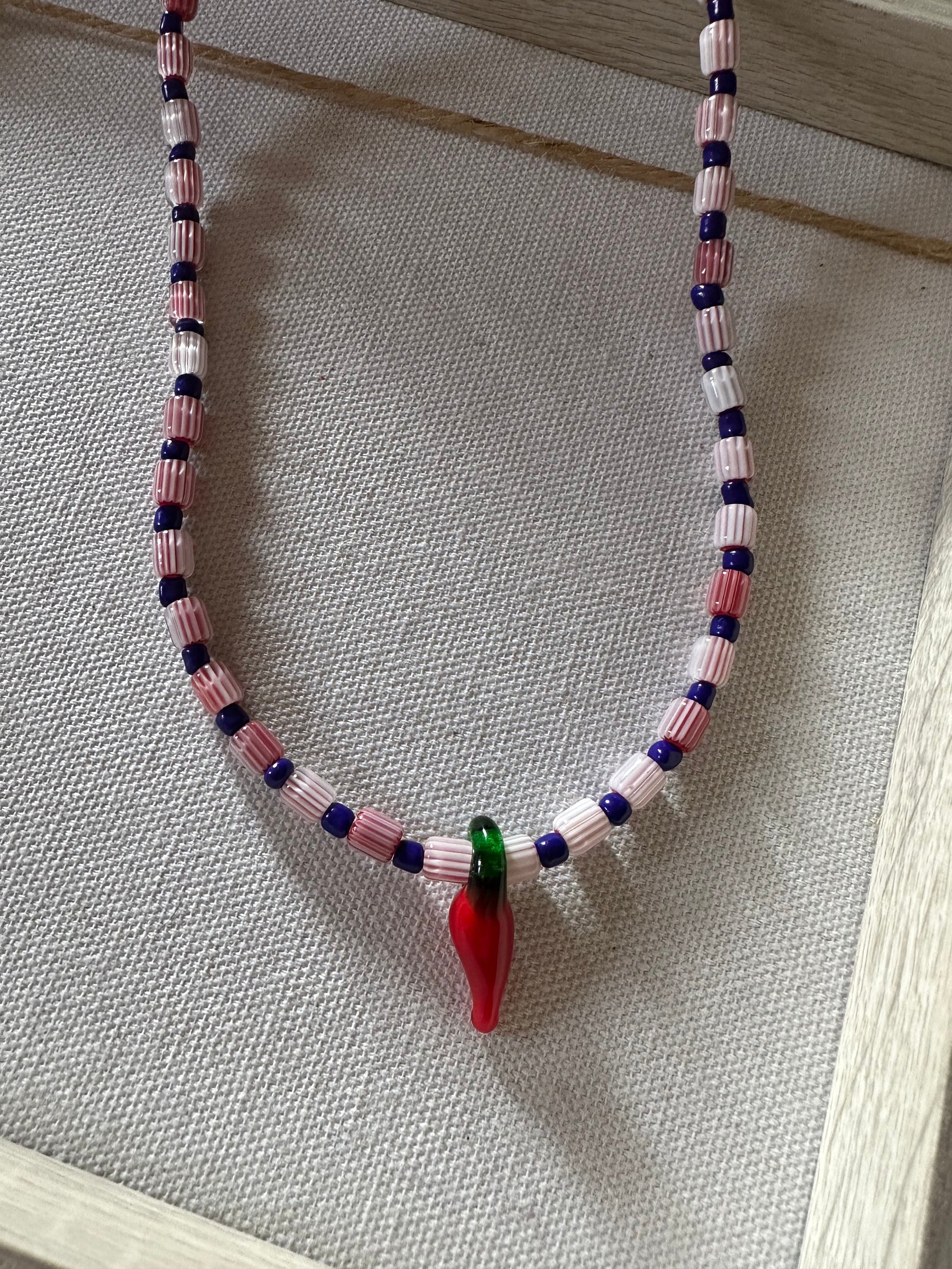 Collar hecho a mano con cuentas de cerámica blancas y cuentas azules, con un abalorio con forma de chili de cristal de murano en color rojo y verde. Cierre ajustable