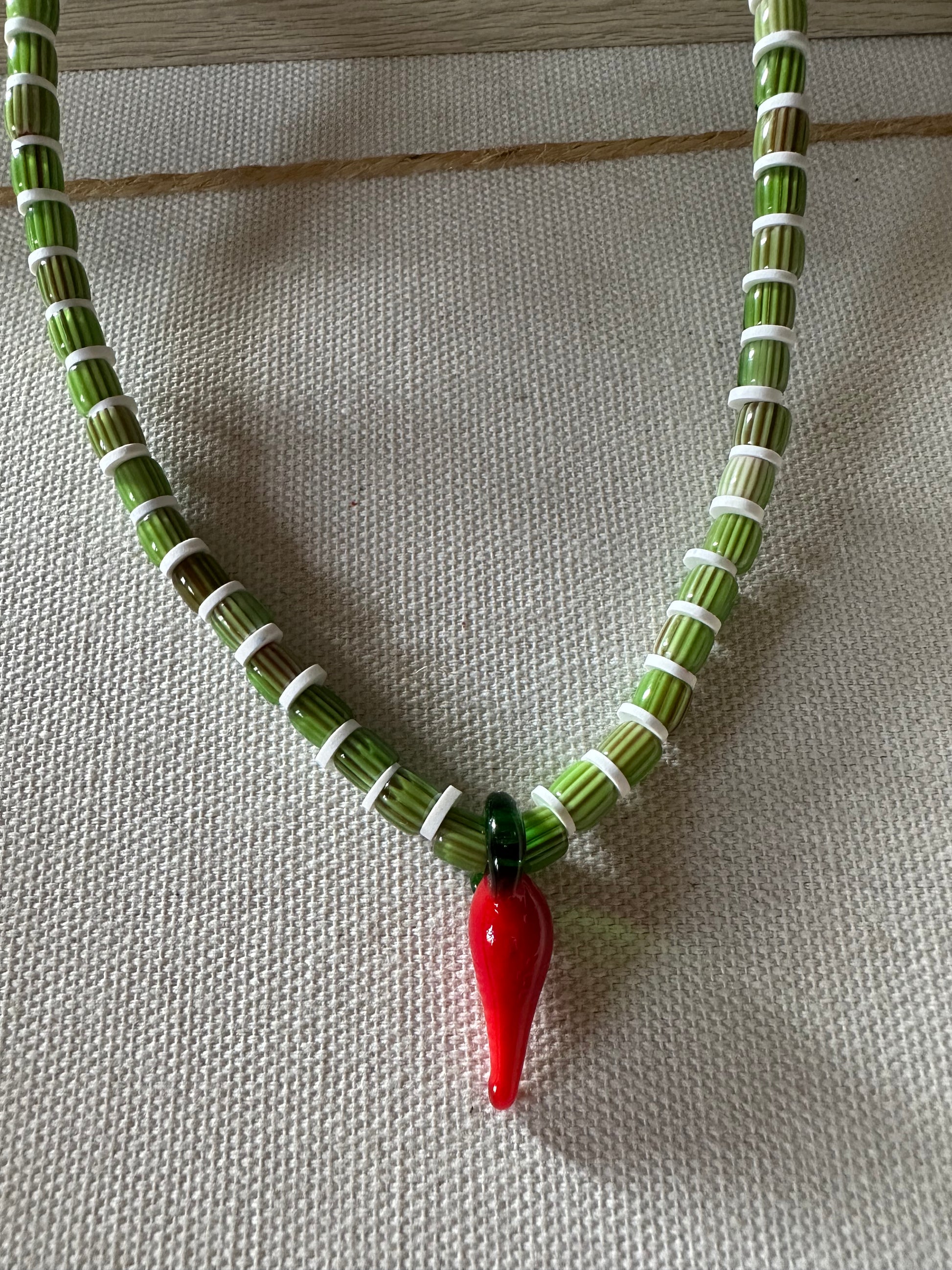 Collar hecho a mano con cuentas de cerámica verdes y arcilla polimérica blanca, con un abalorio con forma de chili de cristal de murano en color rojo y verde. Cierre ajustable