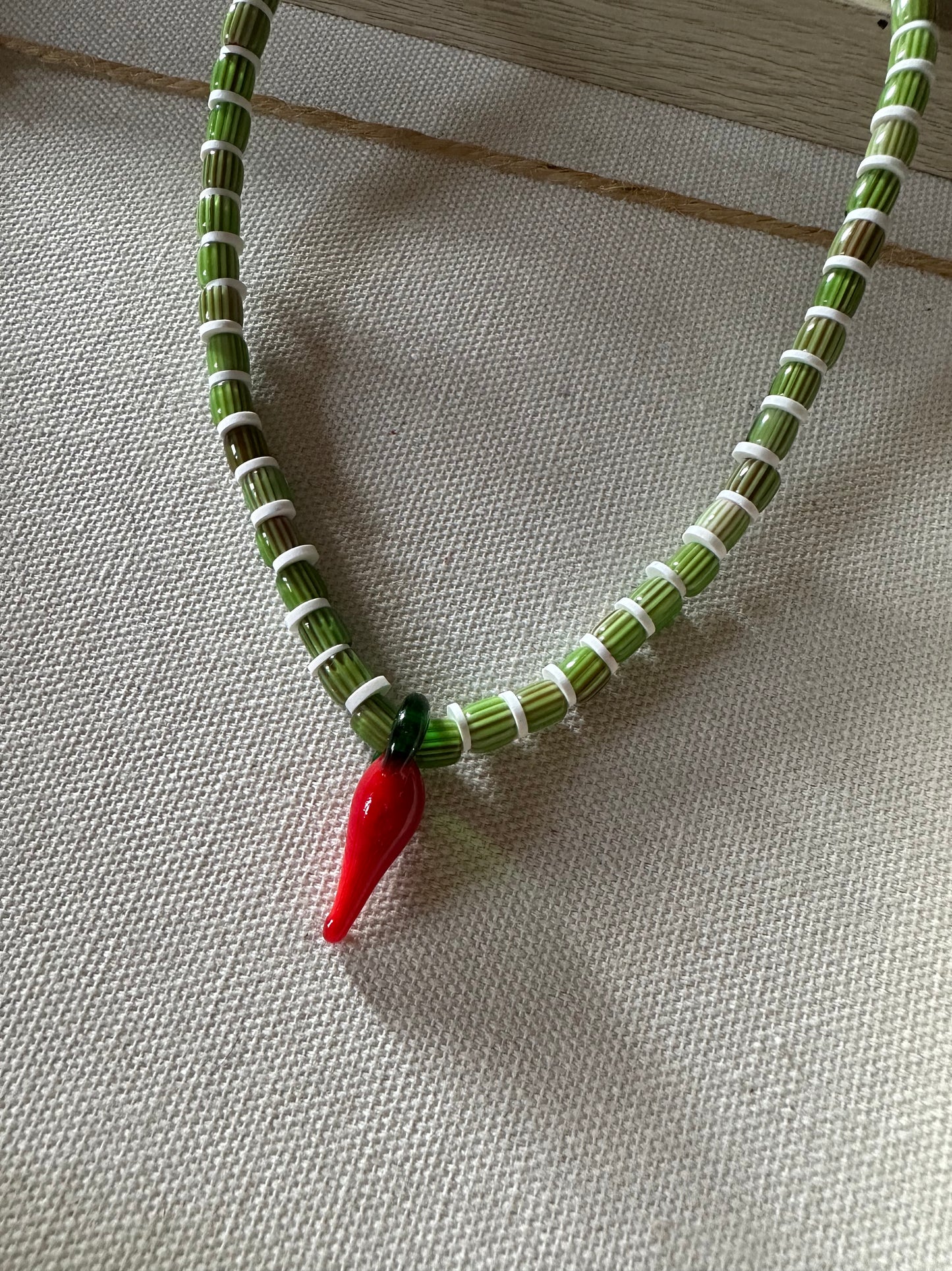 Collar hecho a mano con cuentas de cerámica verdes y arcilla polimérica blanca, con un abalorio con forma de chili de cristal de murano en color rojo y verde. Cierre ajustable