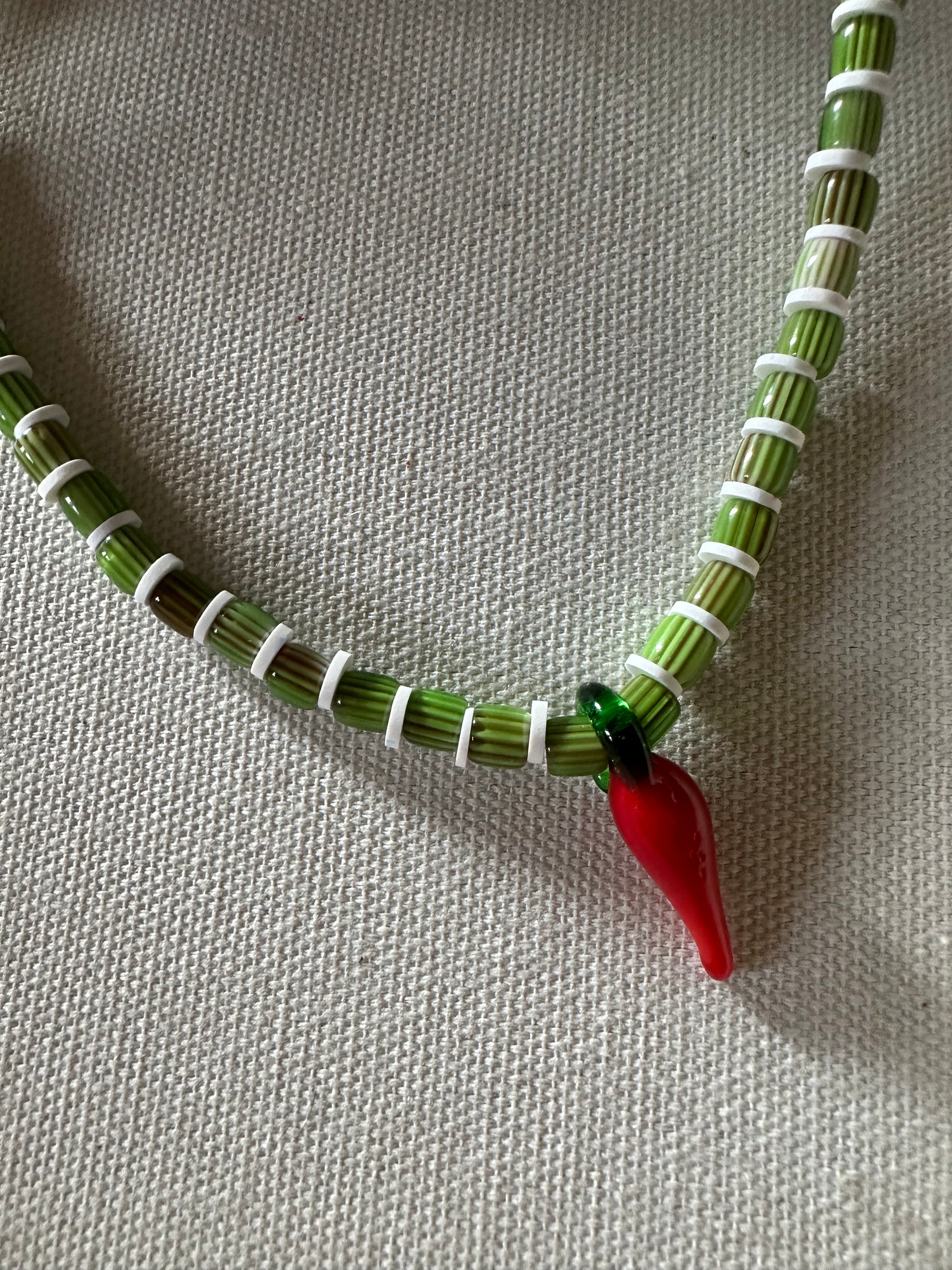 Collar hecho a mano con cuentas de cerámica verdes y arcilla polimérica blanca, con un abalorio con forma de chili de cristal de murano en color rojo y verde. Cierre ajustable