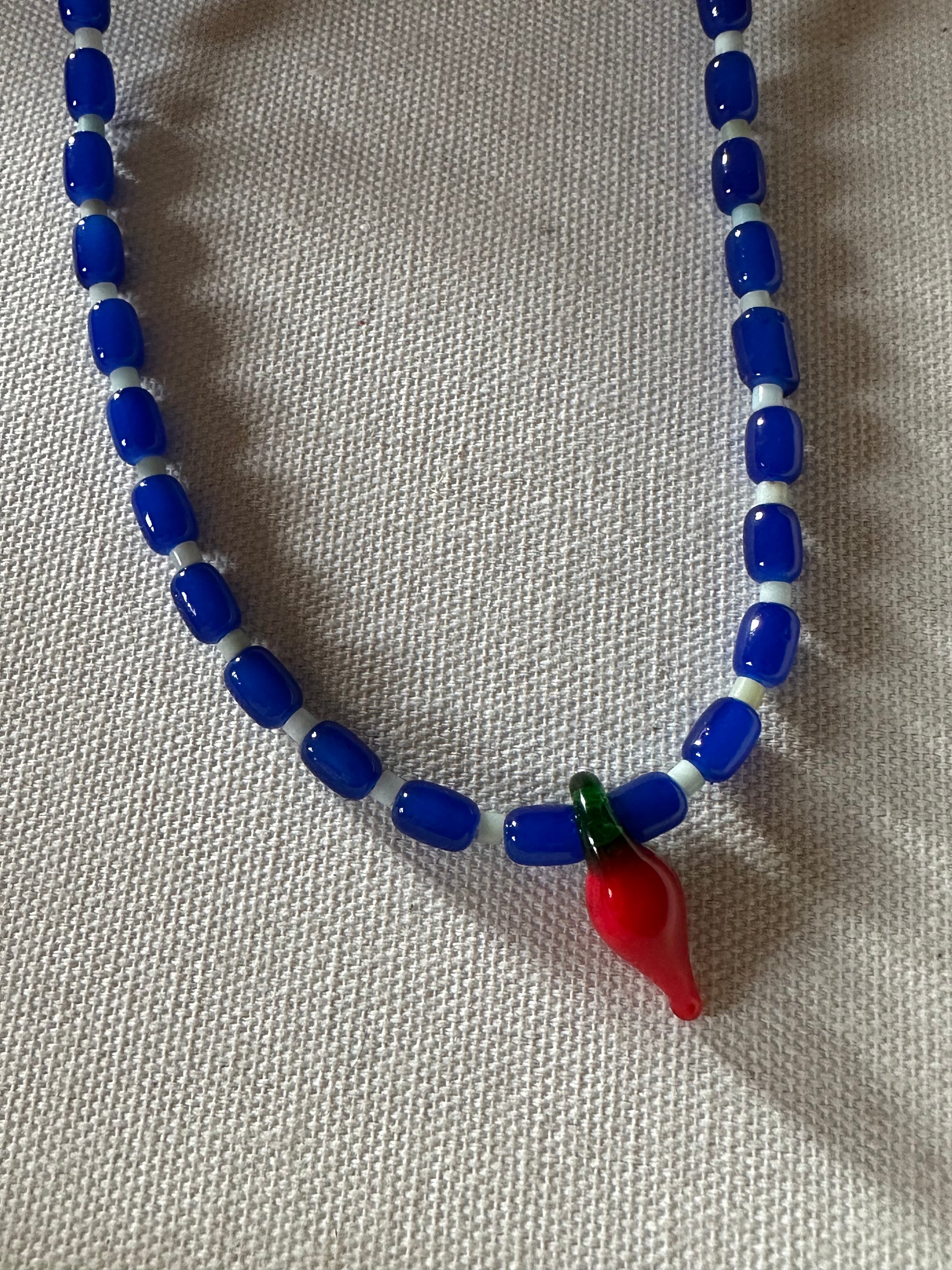 Collar hecho a mano con cuentas de cerámica azul y piedra agatha de árbol, con un abalorio con forma de chili de cristal de murano en color rojo y verde. Cierre ajustable