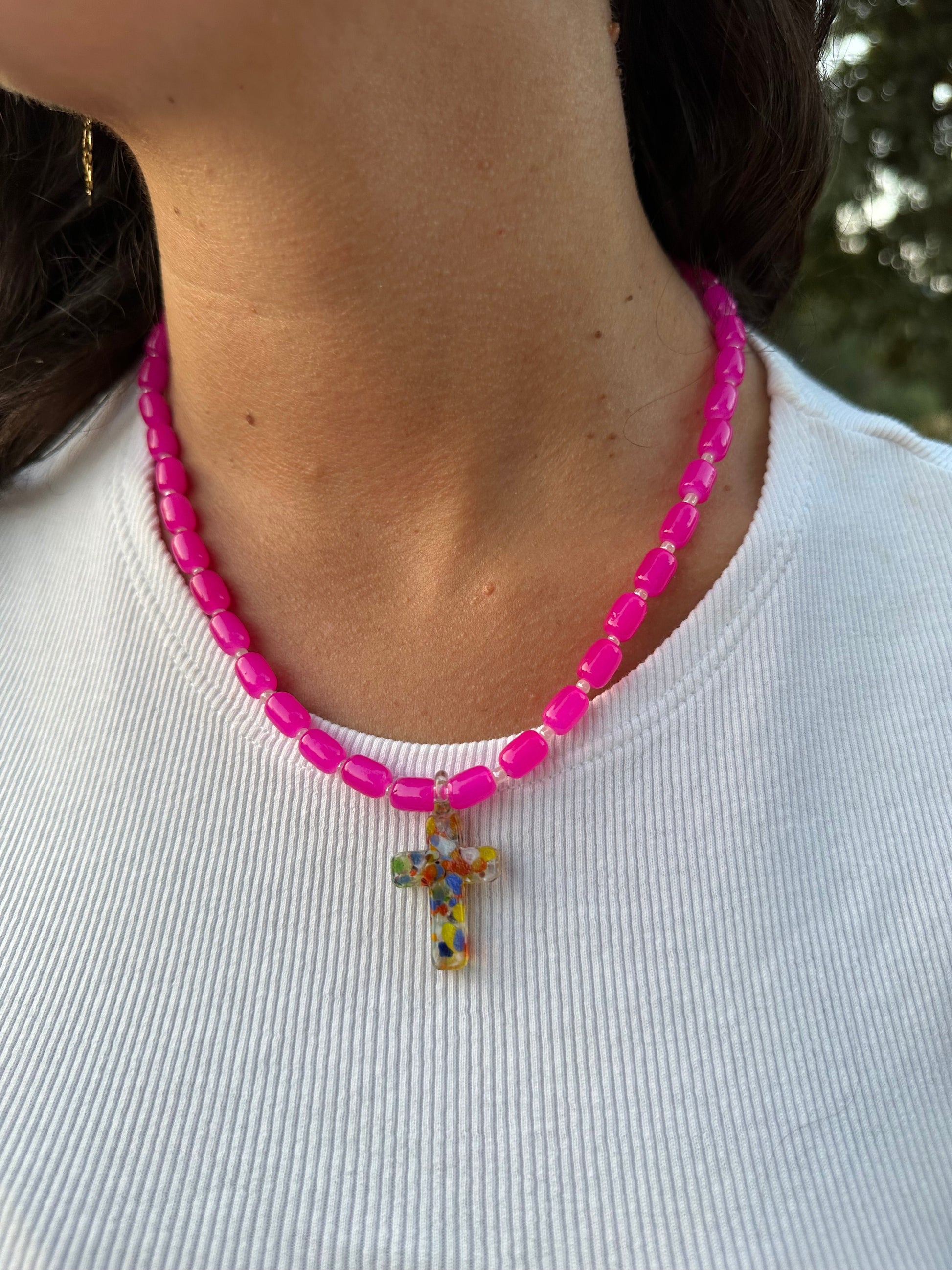 Collar hecho a mano con cuentas de cerámica rosa y con un abalorio con forma de cruz de cristal de murano en varios tonos. Cierre ajustable de acero inoxidable