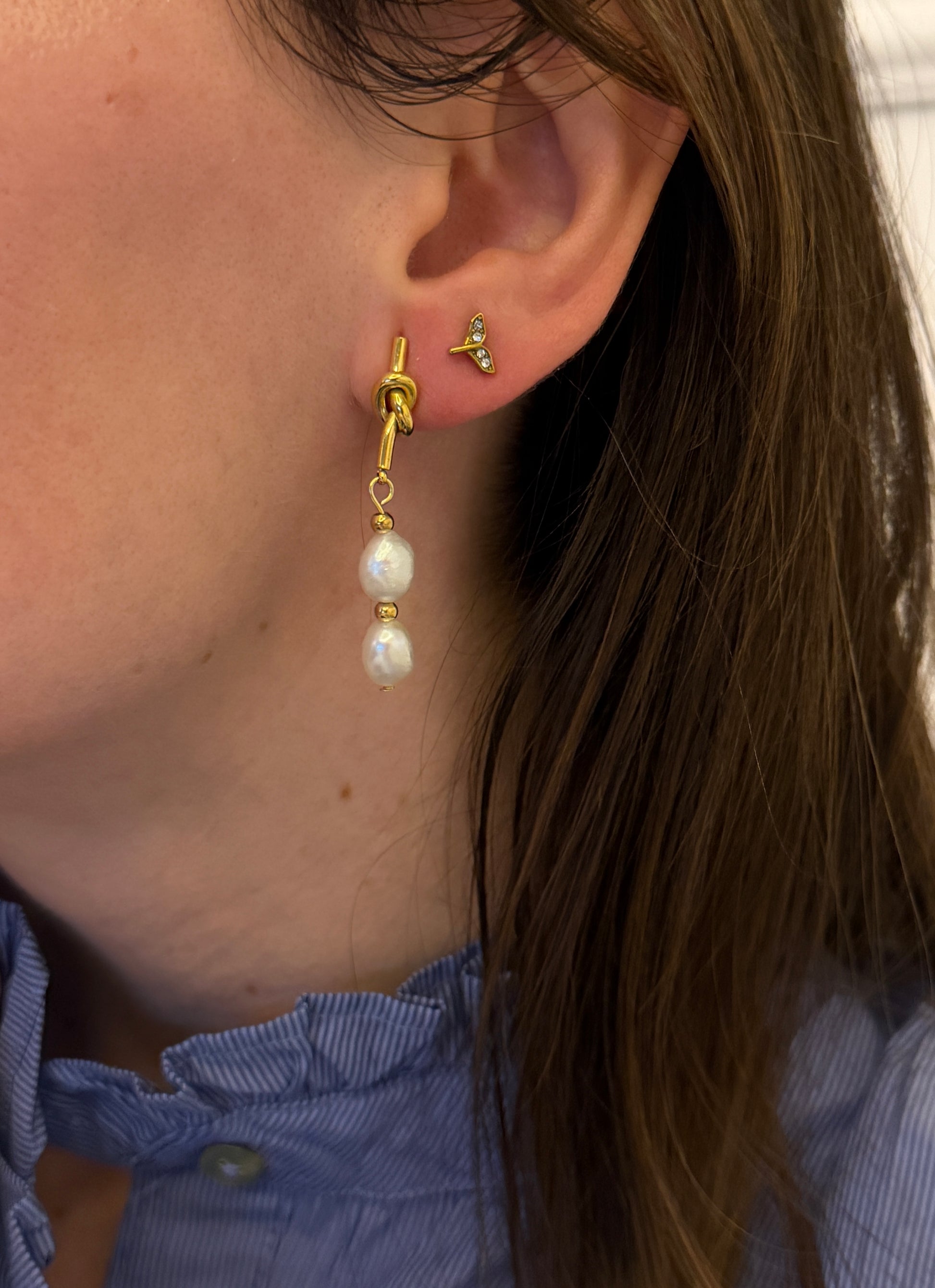 Pendientes de acero inoxidable en color dorado con dos perlas de río. Cierre con forma de nudo. Estos pendientes son perfectos para elevar tus looks. 