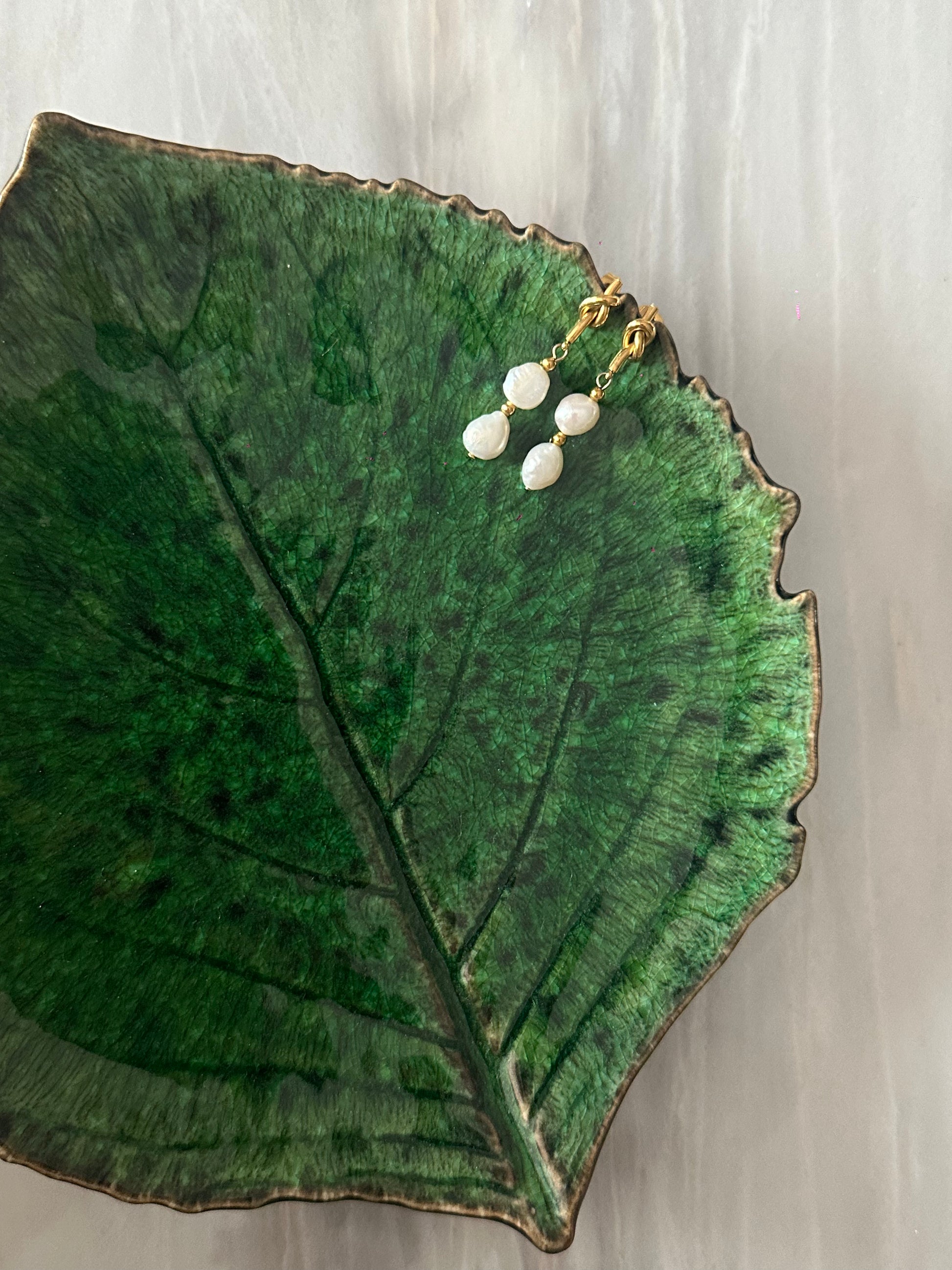 Pendientes de acero inoxidable en color dorado con dos perlas de río. Cierre con forma de nudo. Estos pendientes son perfectos para elevar tus looks. 