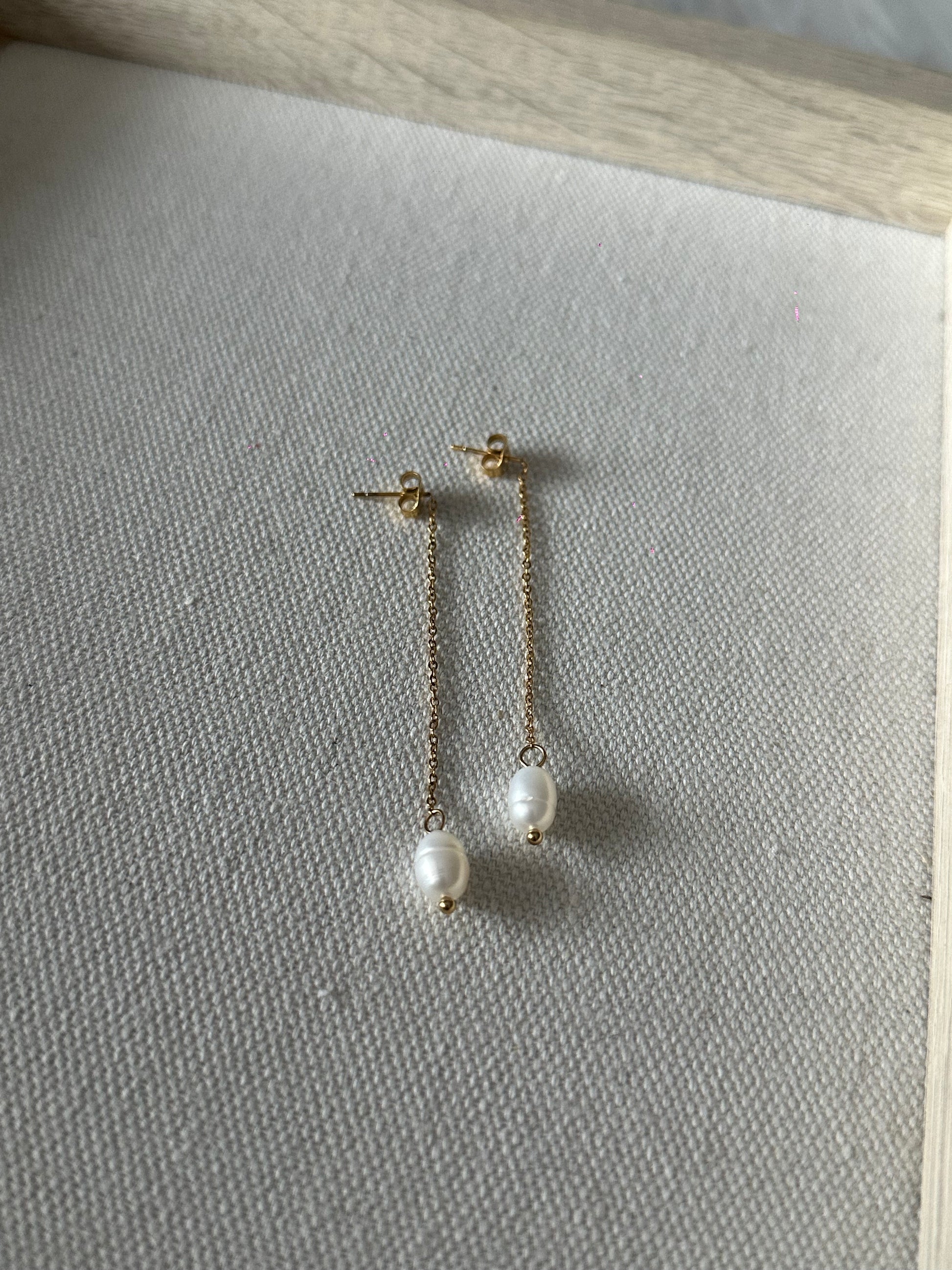 Pendientes largos de acero inoxidable en color dorado con perla de río colgando. Estos pendientes son perfectos para elevar tus looks. 