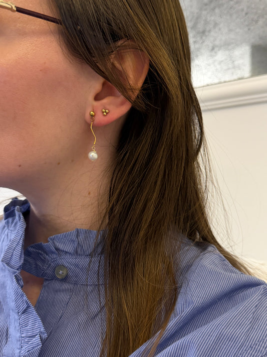 Pendientes de acero inoxidable en color dorado con onda y una perla. Estos pendientes son perfectos para elevar tus looks. 