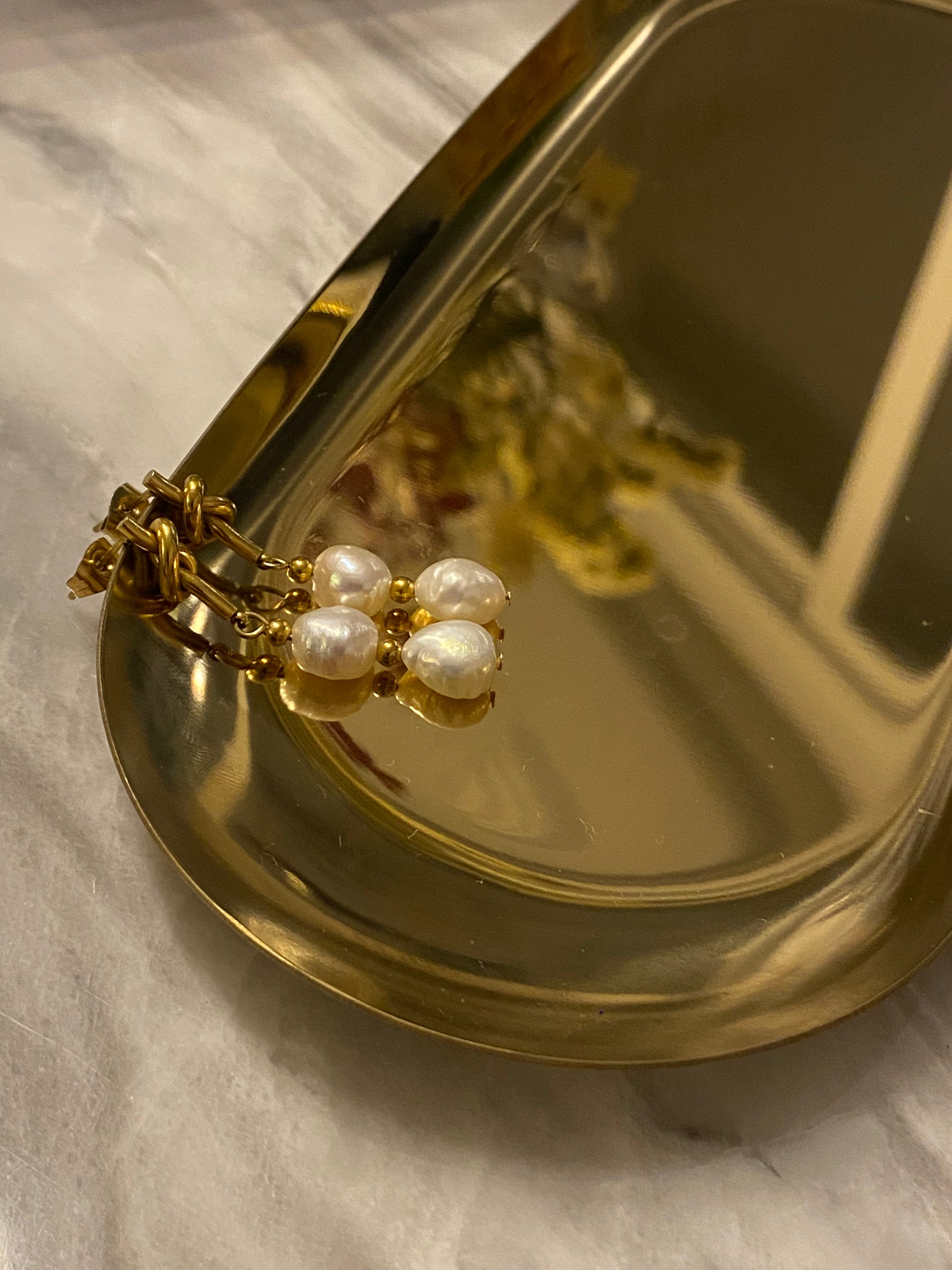 Pendientes de acero inoxidable en color dorado con dos perlas de río. Cierre con forma de nudo. Estos pendientes son perfectos para elevar tus looks. 