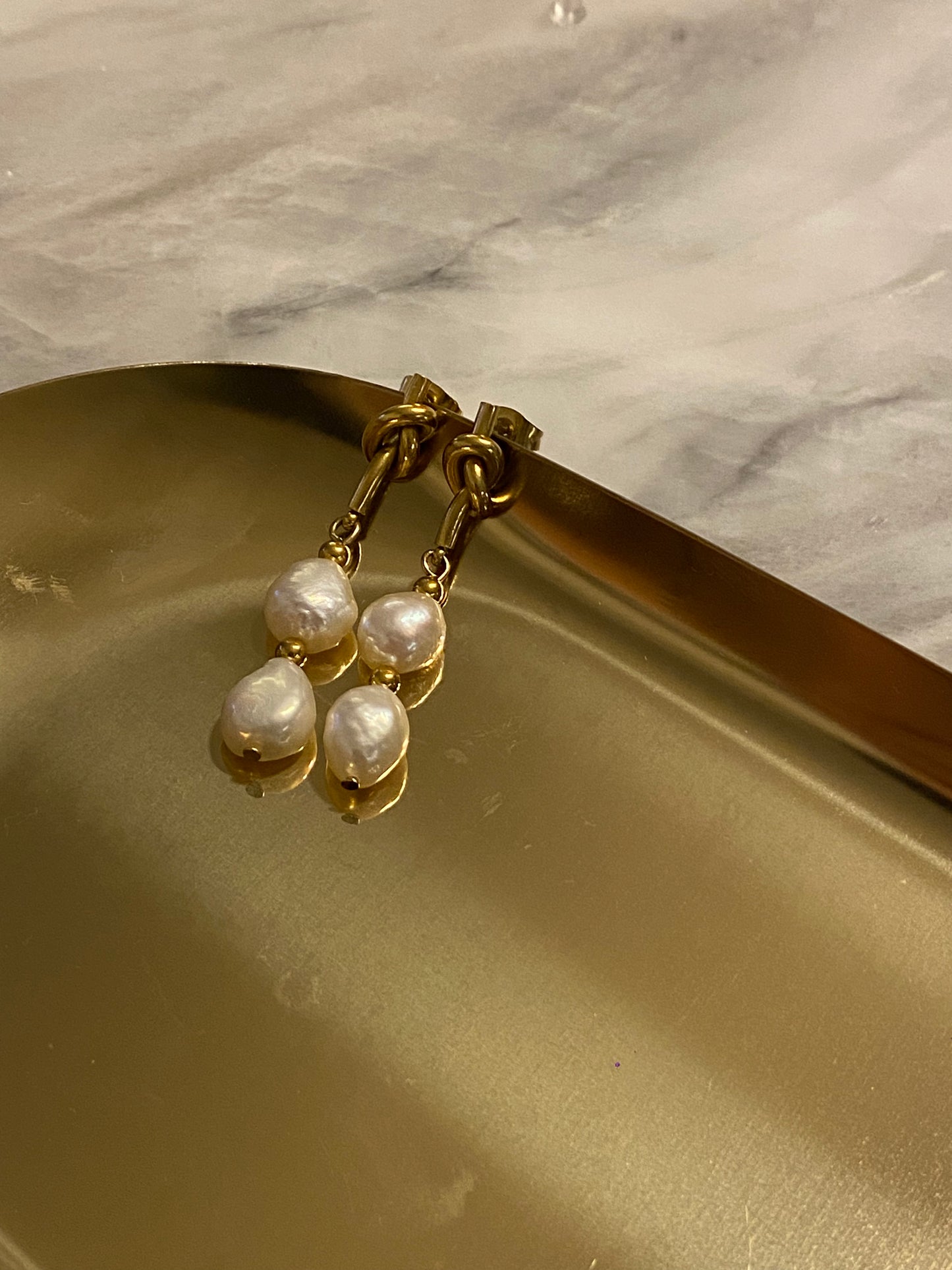 Pendientes de acero inoxidable en color dorado con dos perlas de río. Cierre con forma de nudo. Estos pendientes son perfectos para elevar tus looks. 