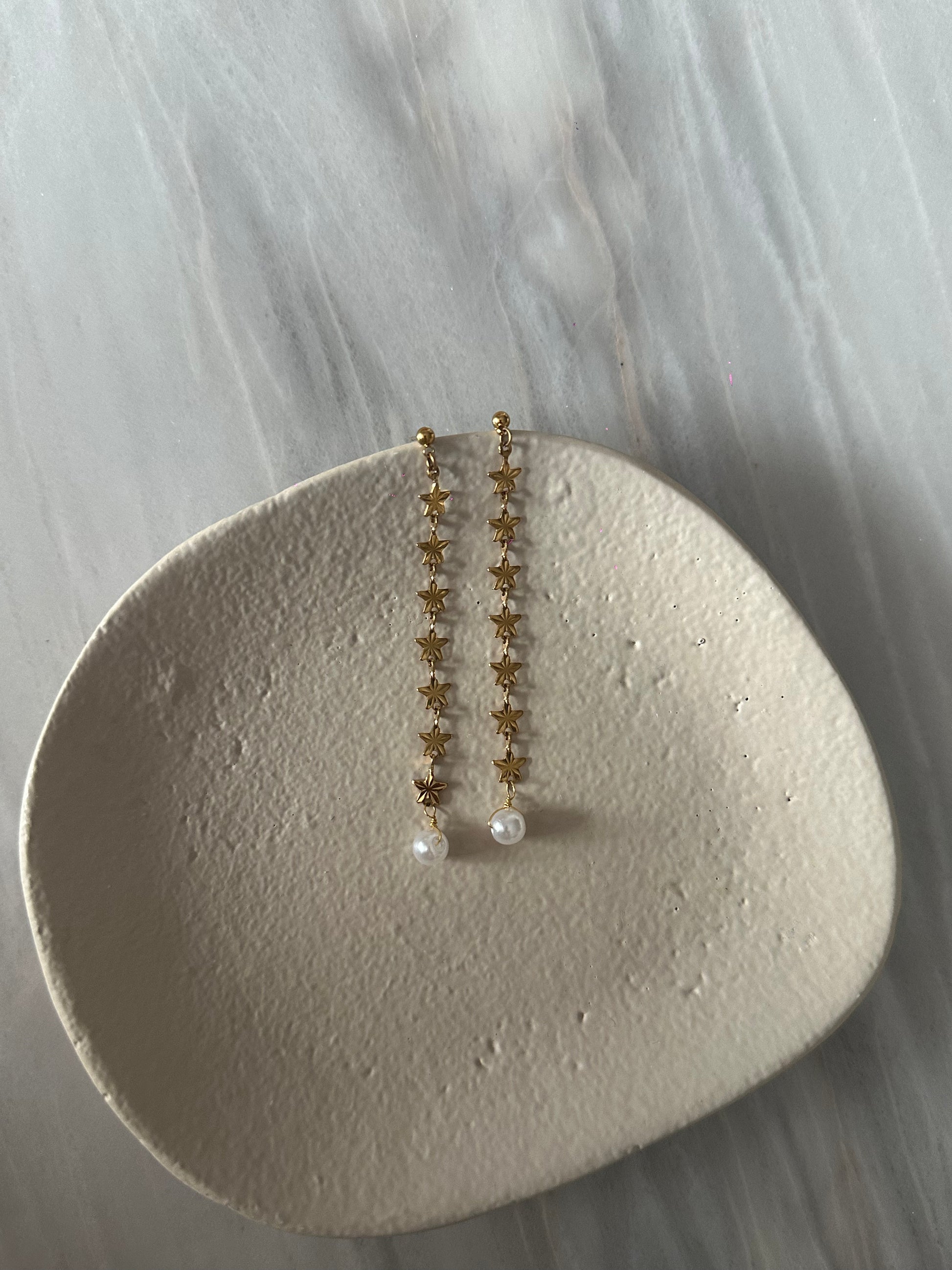 Pendientes de acero inoxidable largos con estrellas doradas y una perla. Estos pendientes son perfectos para elevar tus looks. 