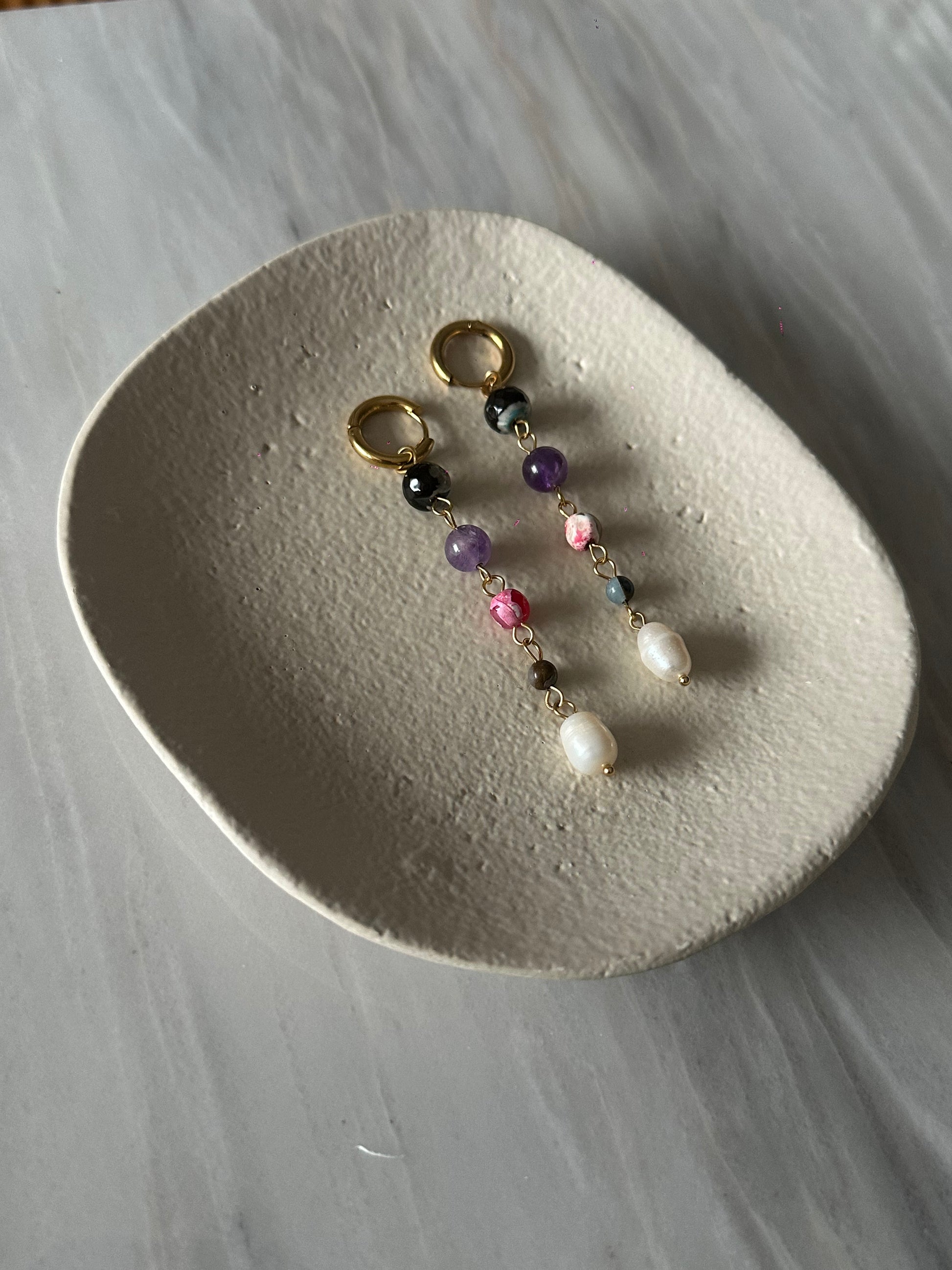 Pendientes de acero inoxidable en color dorado largos con piedras de colores y una perla. Estos pendientes son perfectos para elevar tus looks. 