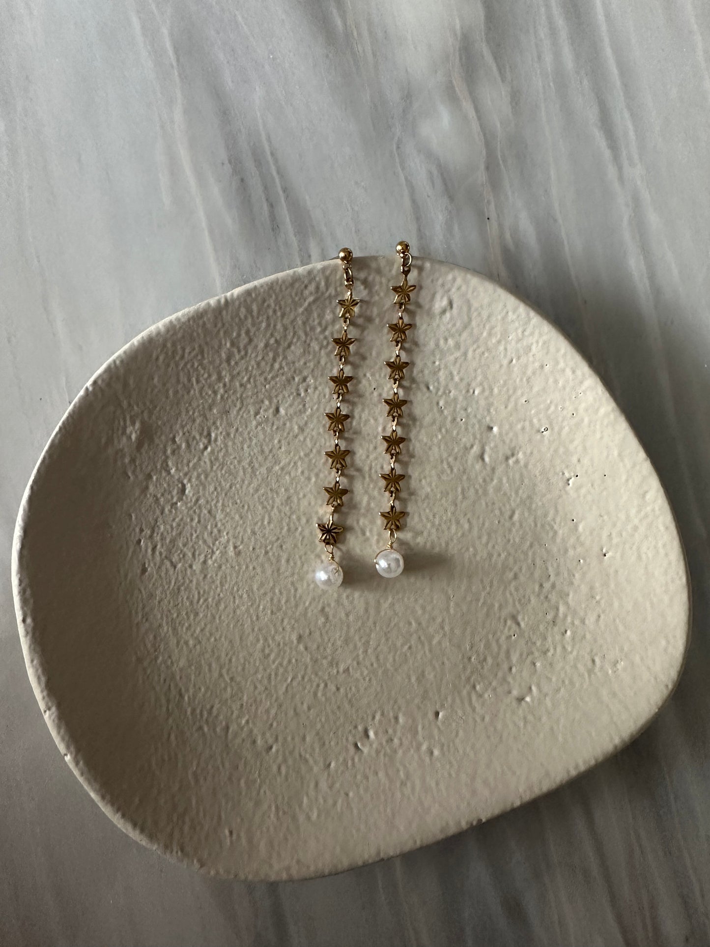 Pendientes de acero inoxidable largos con estrellas doradas y una perla. Estos pendientes son perfectos para elevar tus looks. 